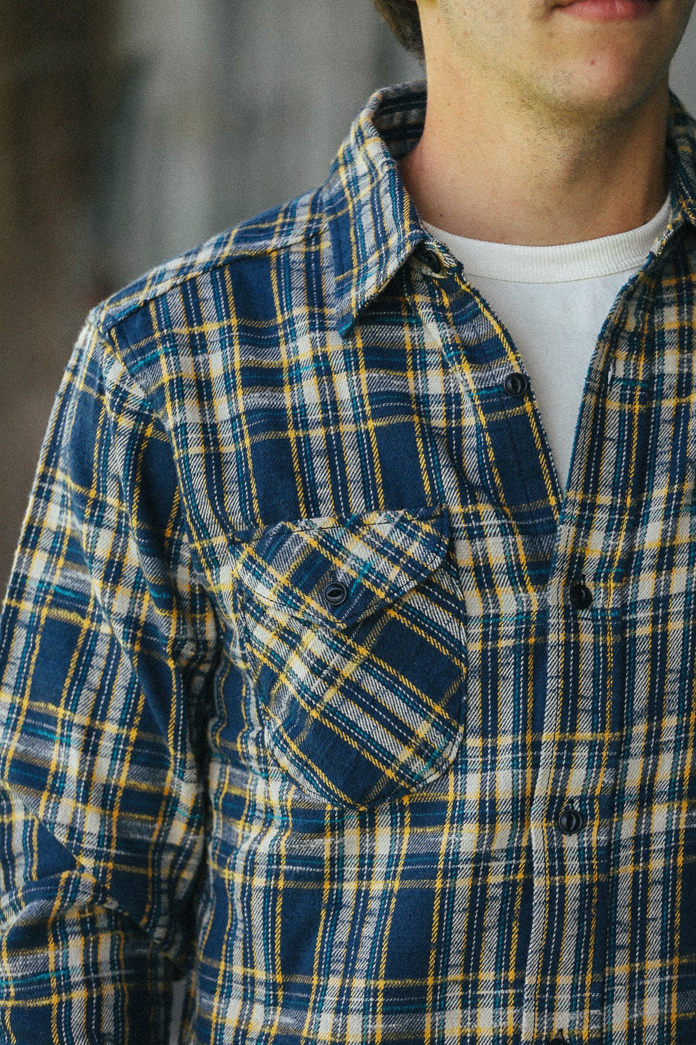 A close-up of a person wearing a blue, yellow, and white plaid button-up shirt over a white undershirt.