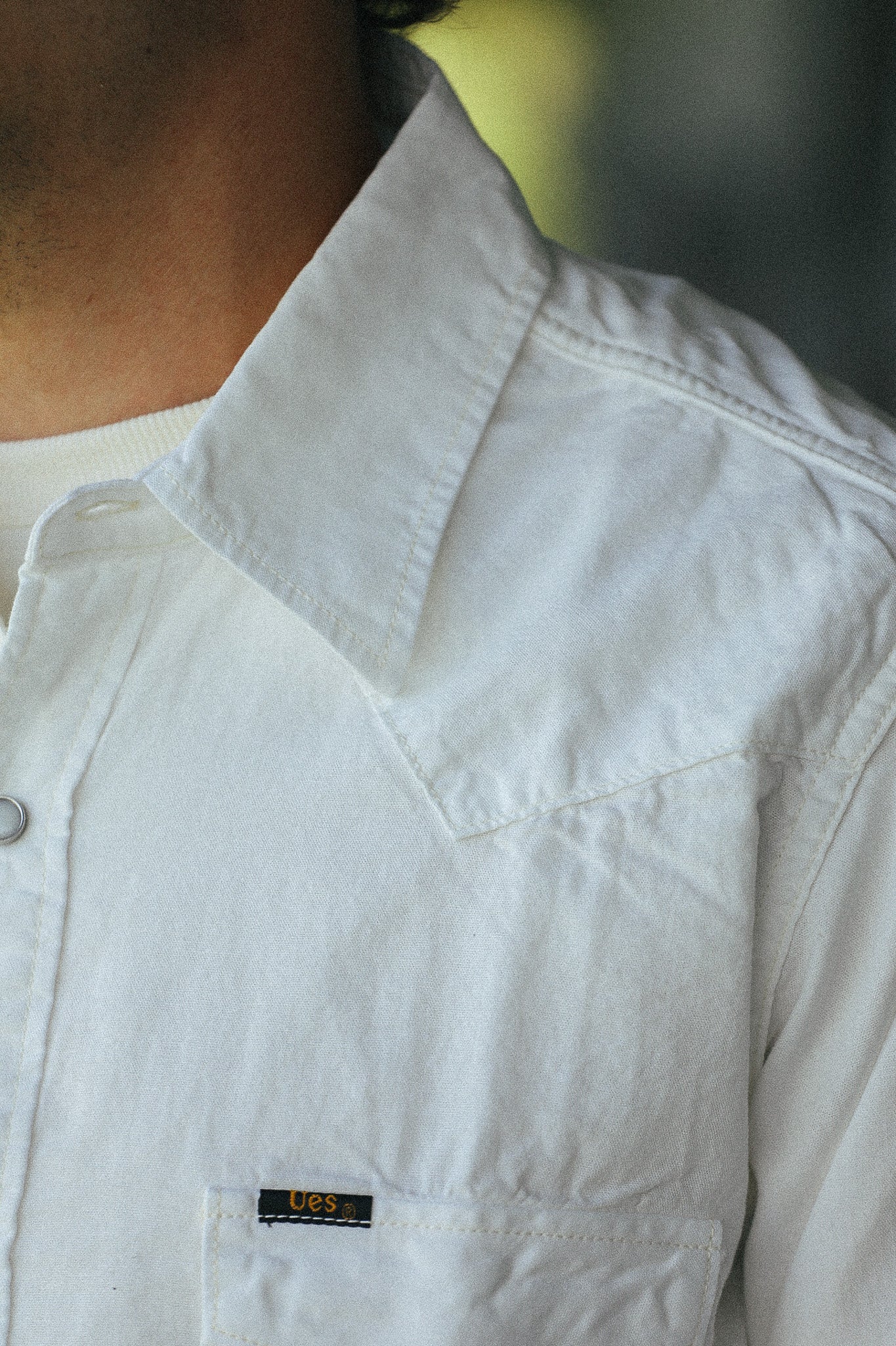 Close-up of a person wearing a white western-style button-up shirt with a pointed collar and a small black U.S.