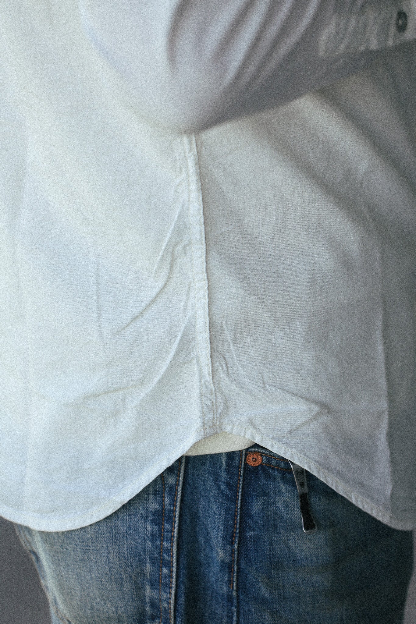 Close-up of a person wearing a white long-sleeve button-up shirt tucked into blue jeans, showing the side and back drape of the shirt.