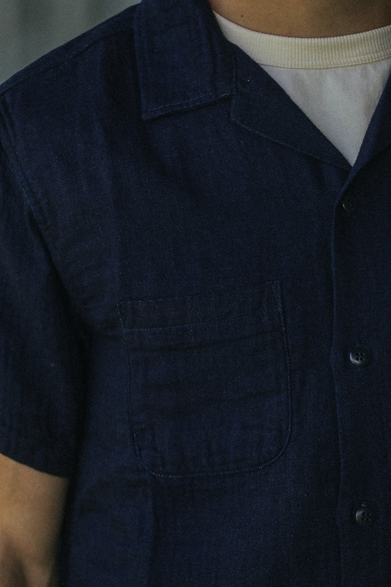 Close-up of a person wearing a dark navy short-sleeve button-front shirt with a chest pocket over a white crew-neck undershirt.