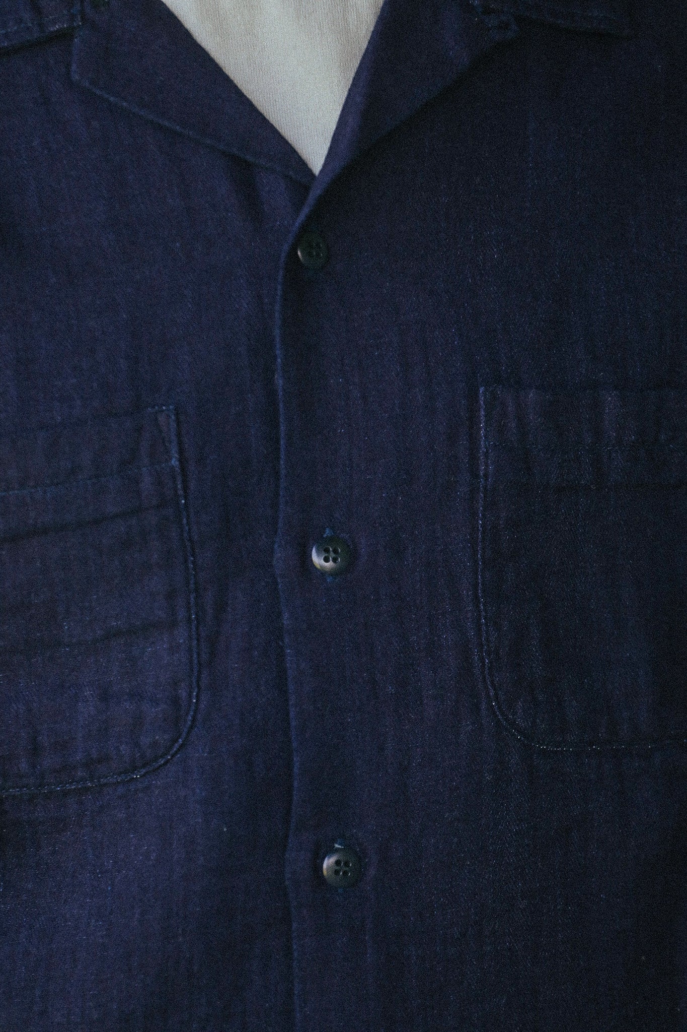 Close-up of a dark navy blue linen shirt with a button-down front, featuring two chest pockets and a pointed collar.