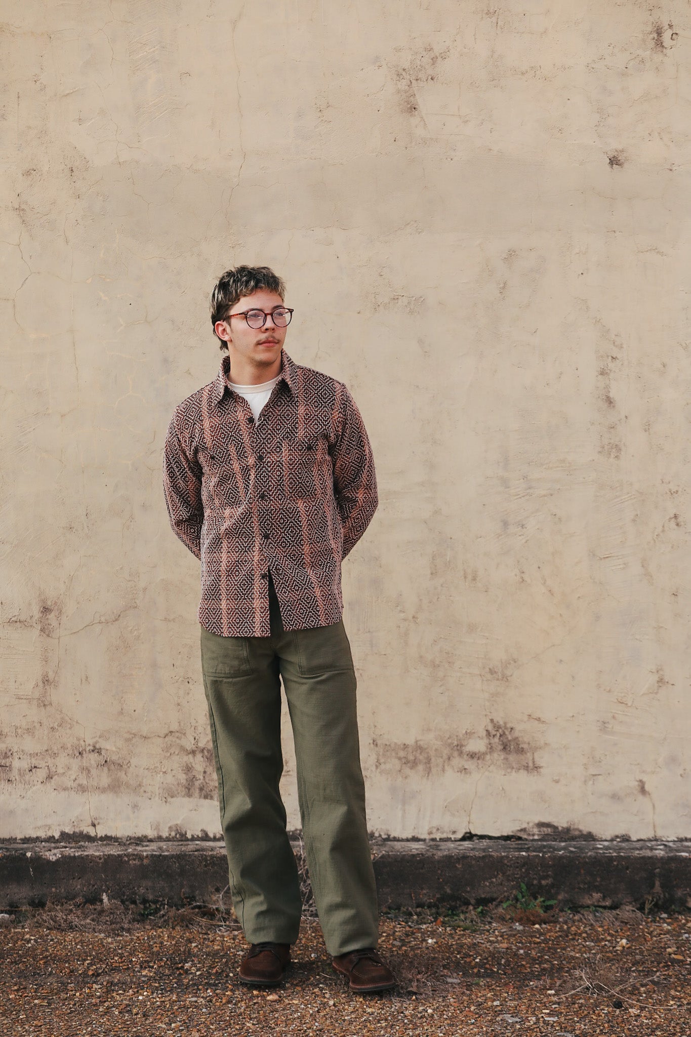 Person wearing a patterned shirt over a plain shirt with a beige background
