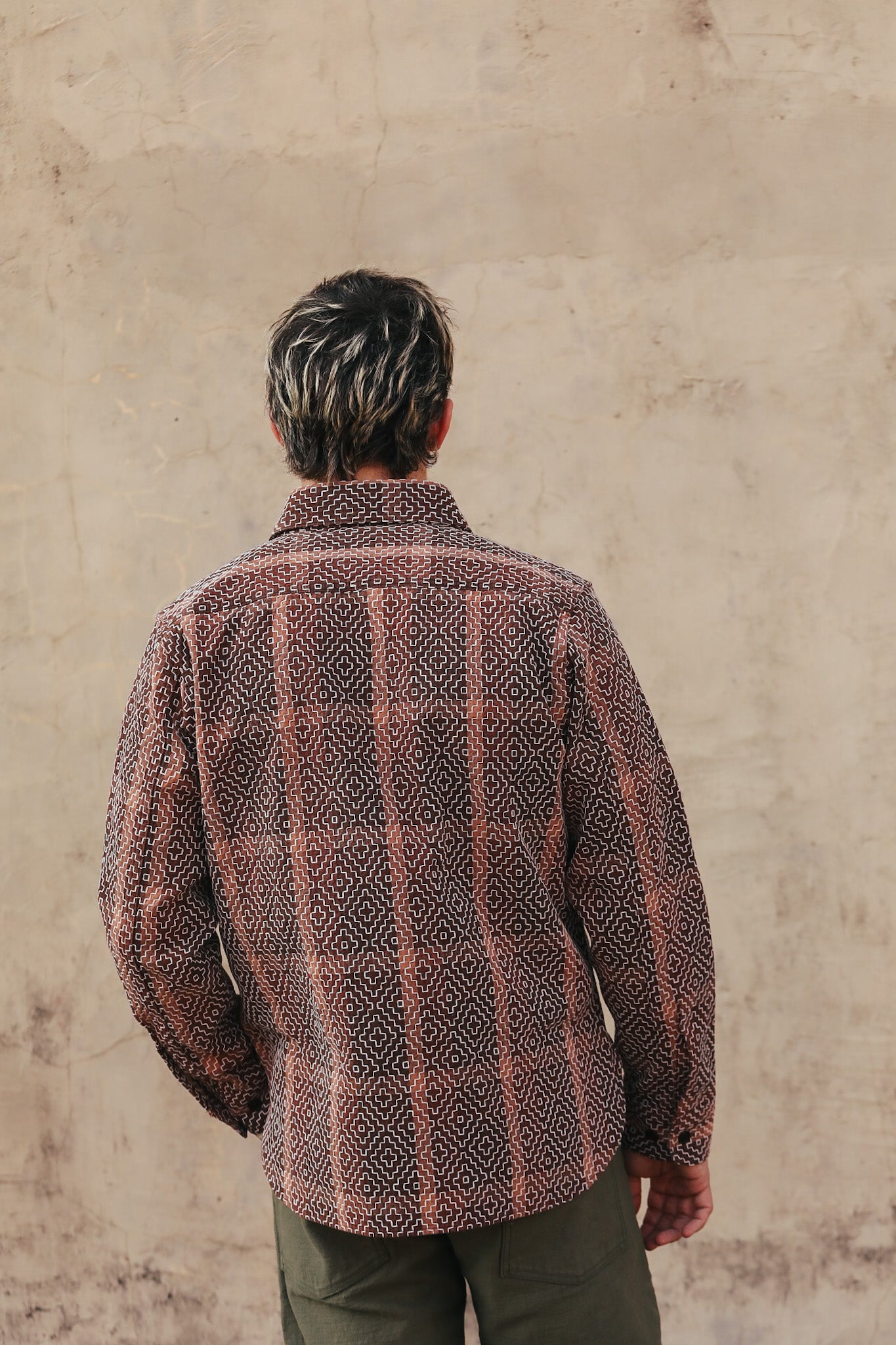 Person wearing a patterned jacket against a beige wall