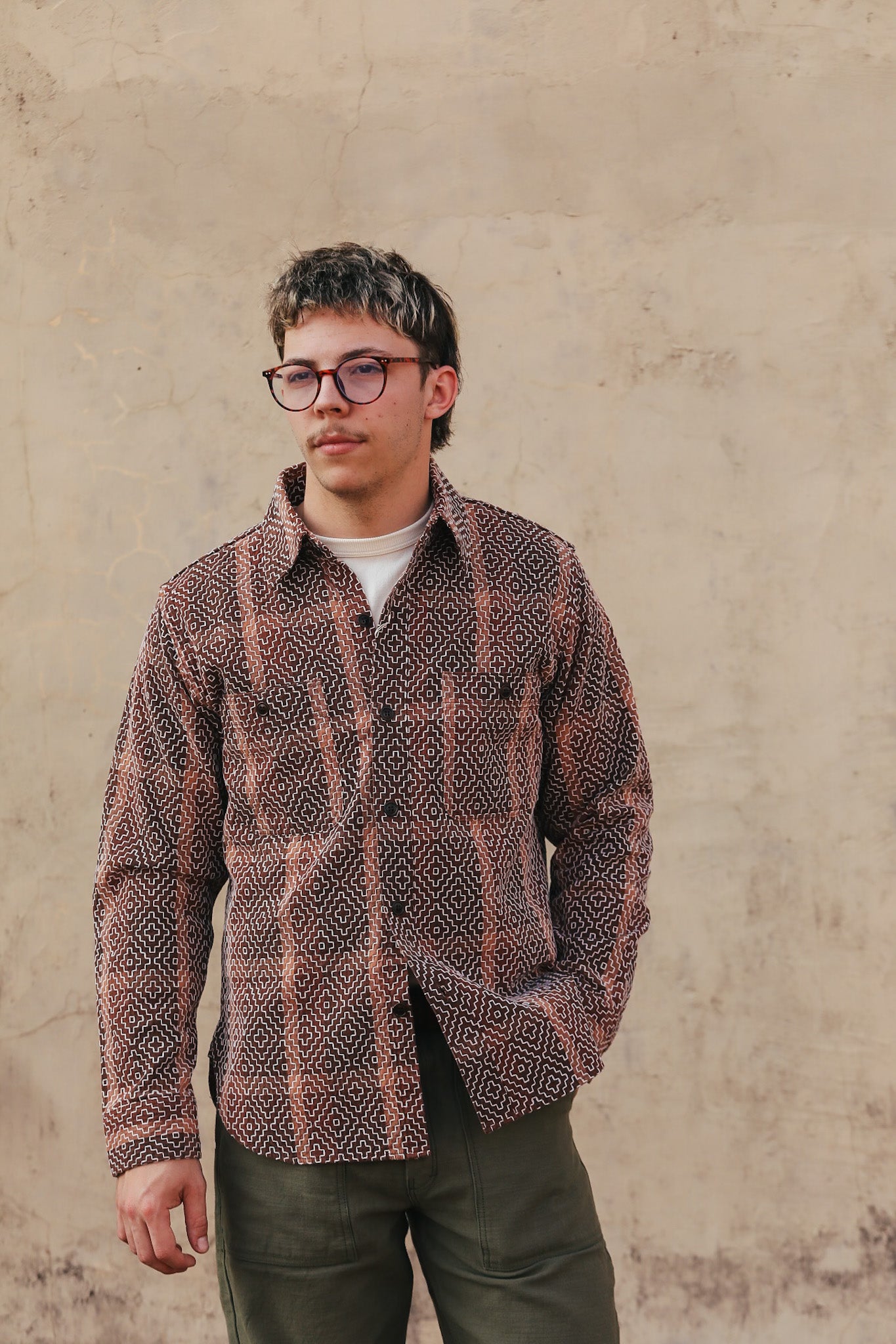 Person wearing a patterned shirt over a plain shirt with a beige background