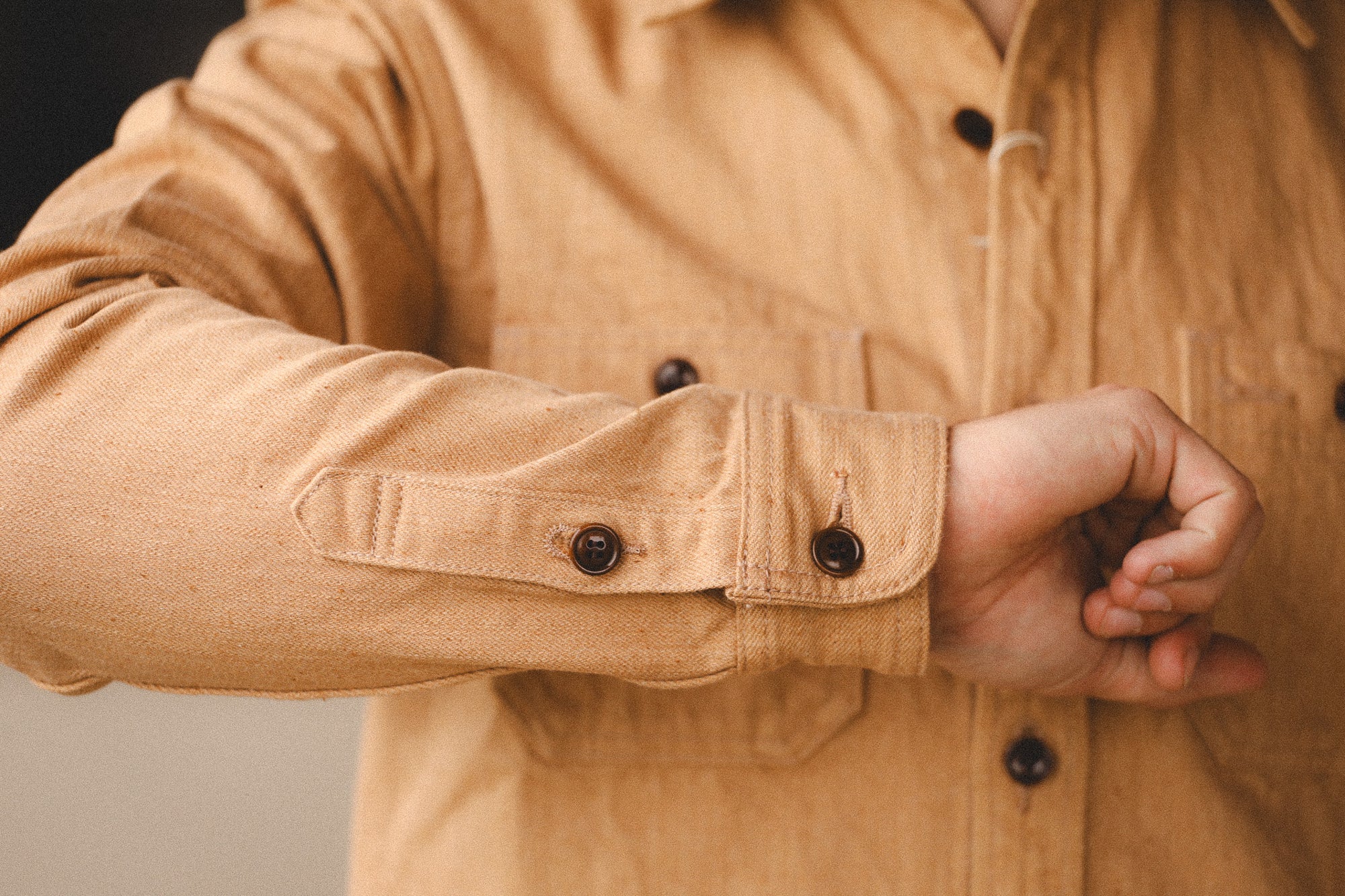Close-up of a person wearing a beige jacket with button details.