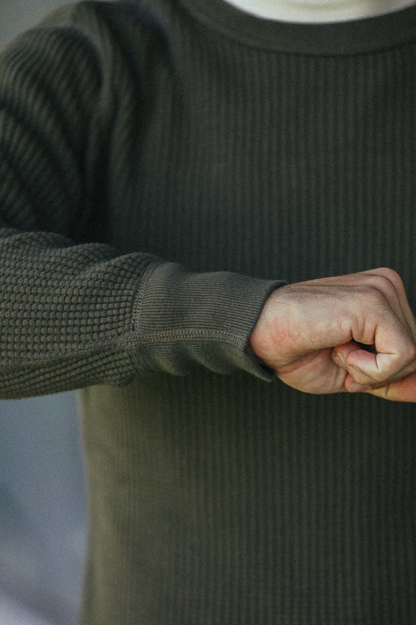 Close-up of a person wearing a dark olive green ribbed knit sweater, showing the sleeve cuff and hand.