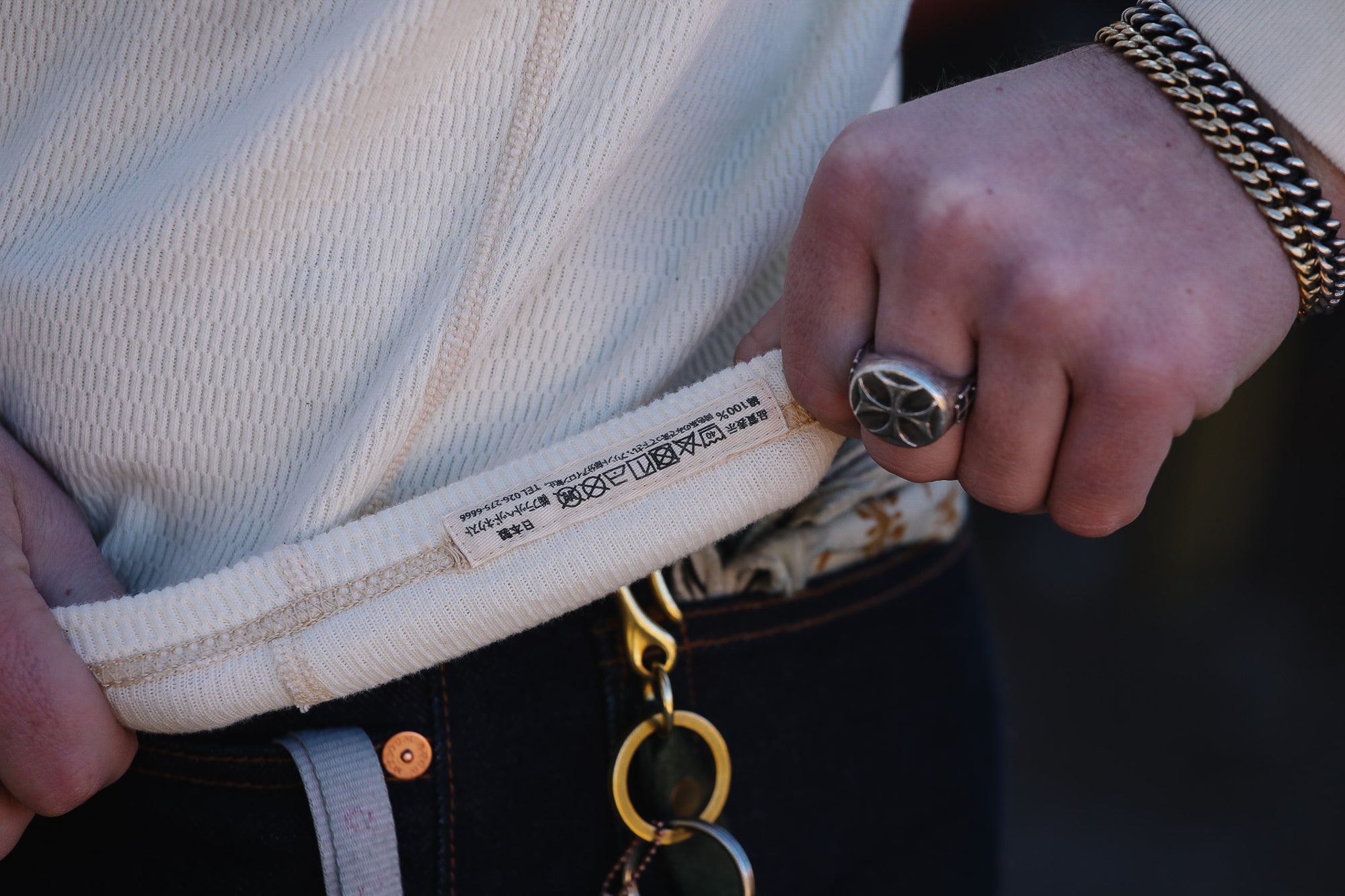 Person holding a white product packaging with text, wearing a gold chain and ring.