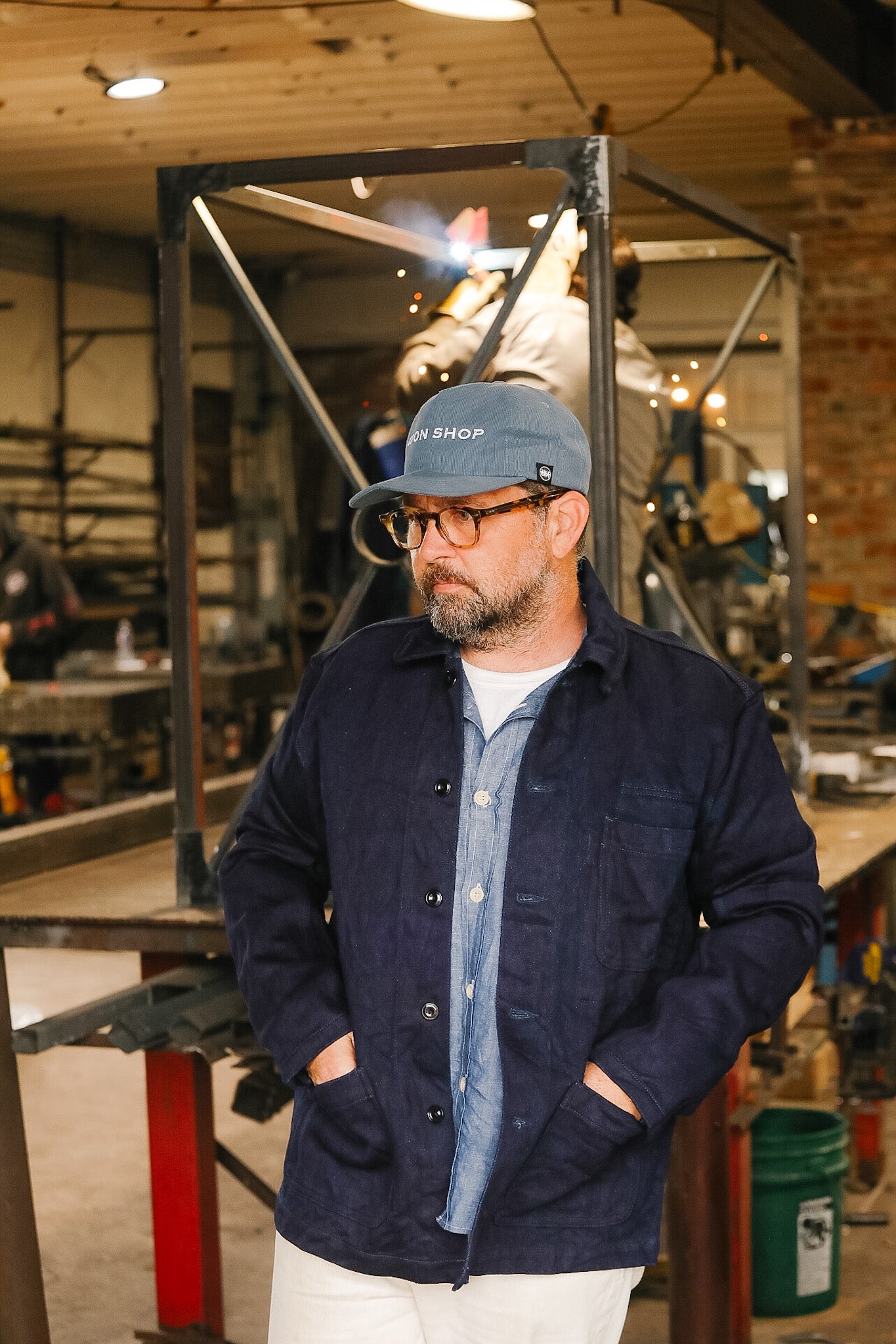 Man wearing a blue cap and dark jacket in a workshop setting