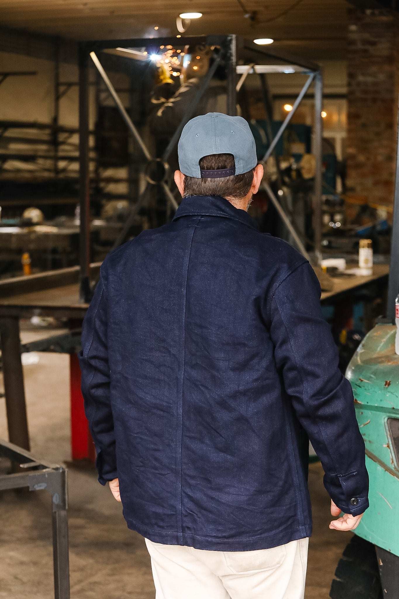 Person wearing a navy jacket and cap in a workshop setting