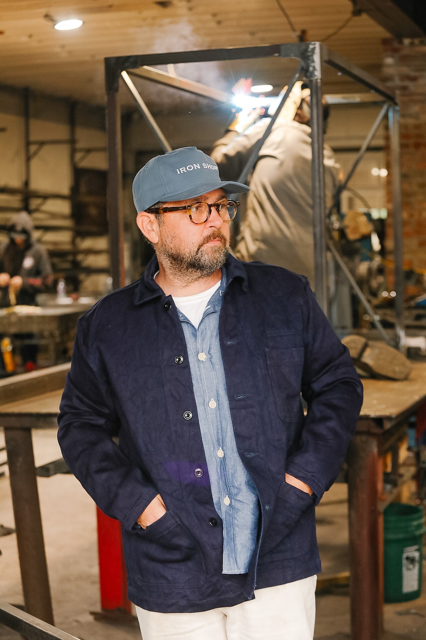 Man wearing a navy jacket and blue cap in a workshop setting