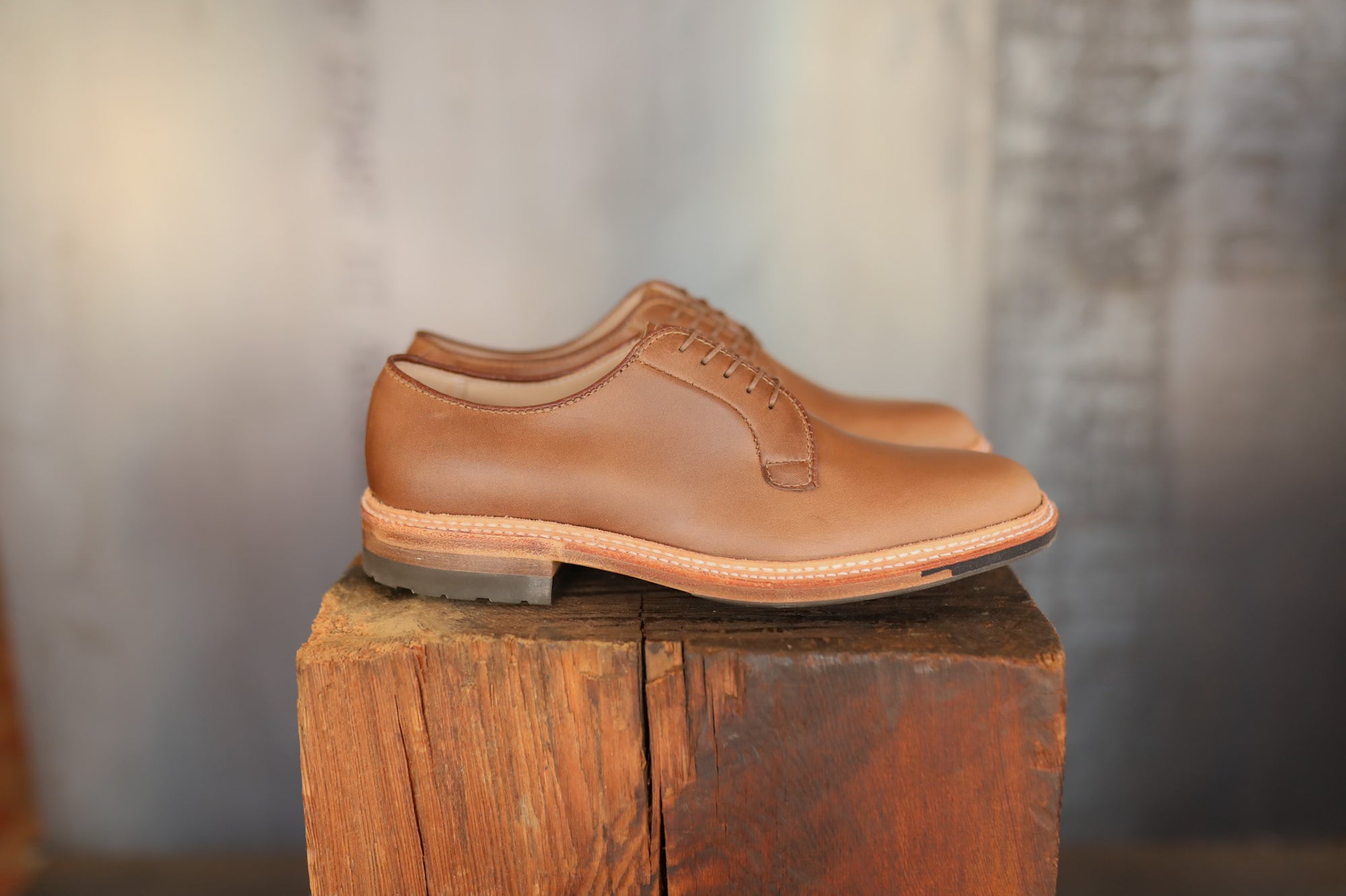 Pair of brown leather shoes on a wooden block with a neutral background