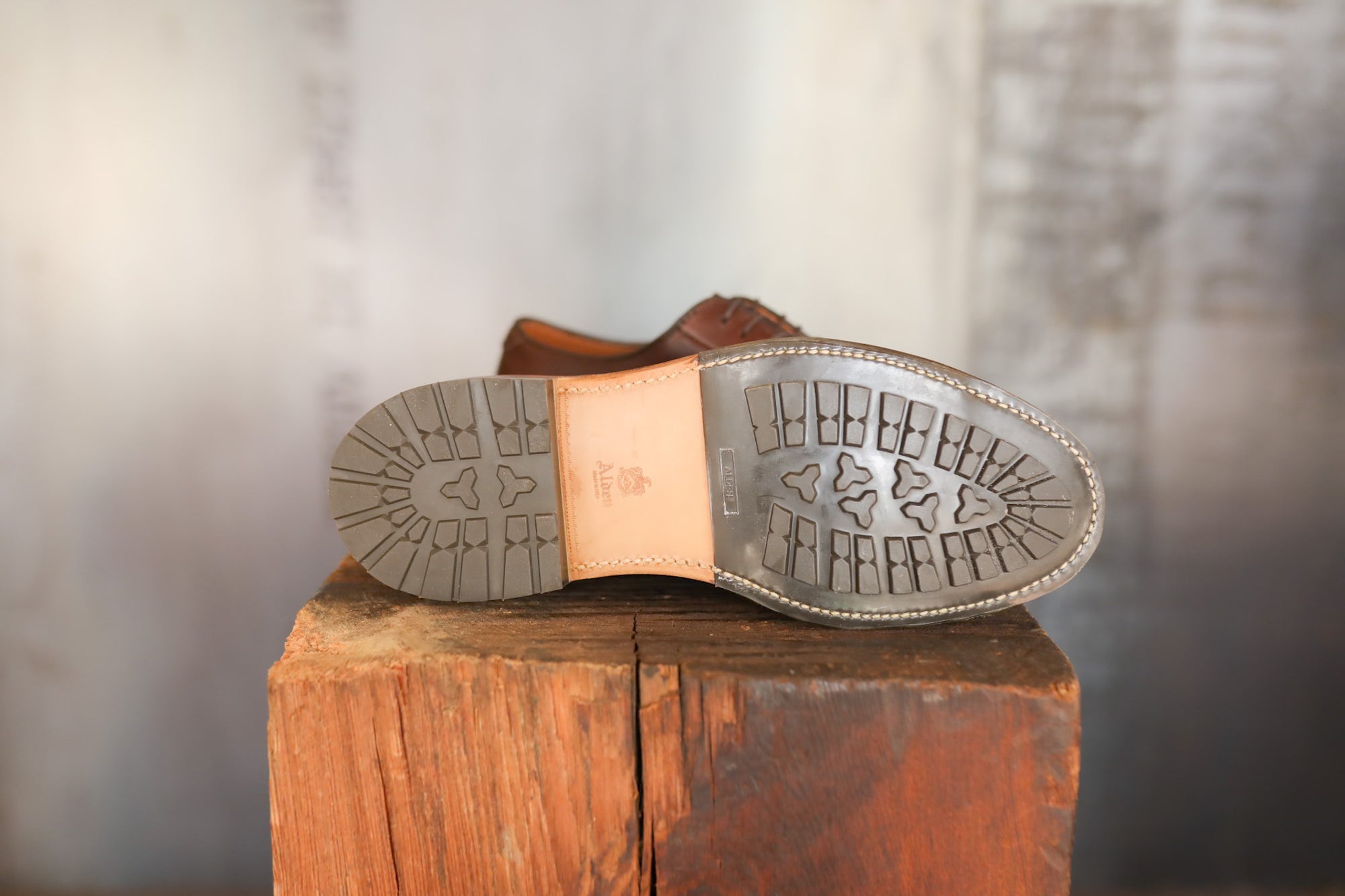 Brown leather shoe sole with tread pattern on a wooden block against a blurred background