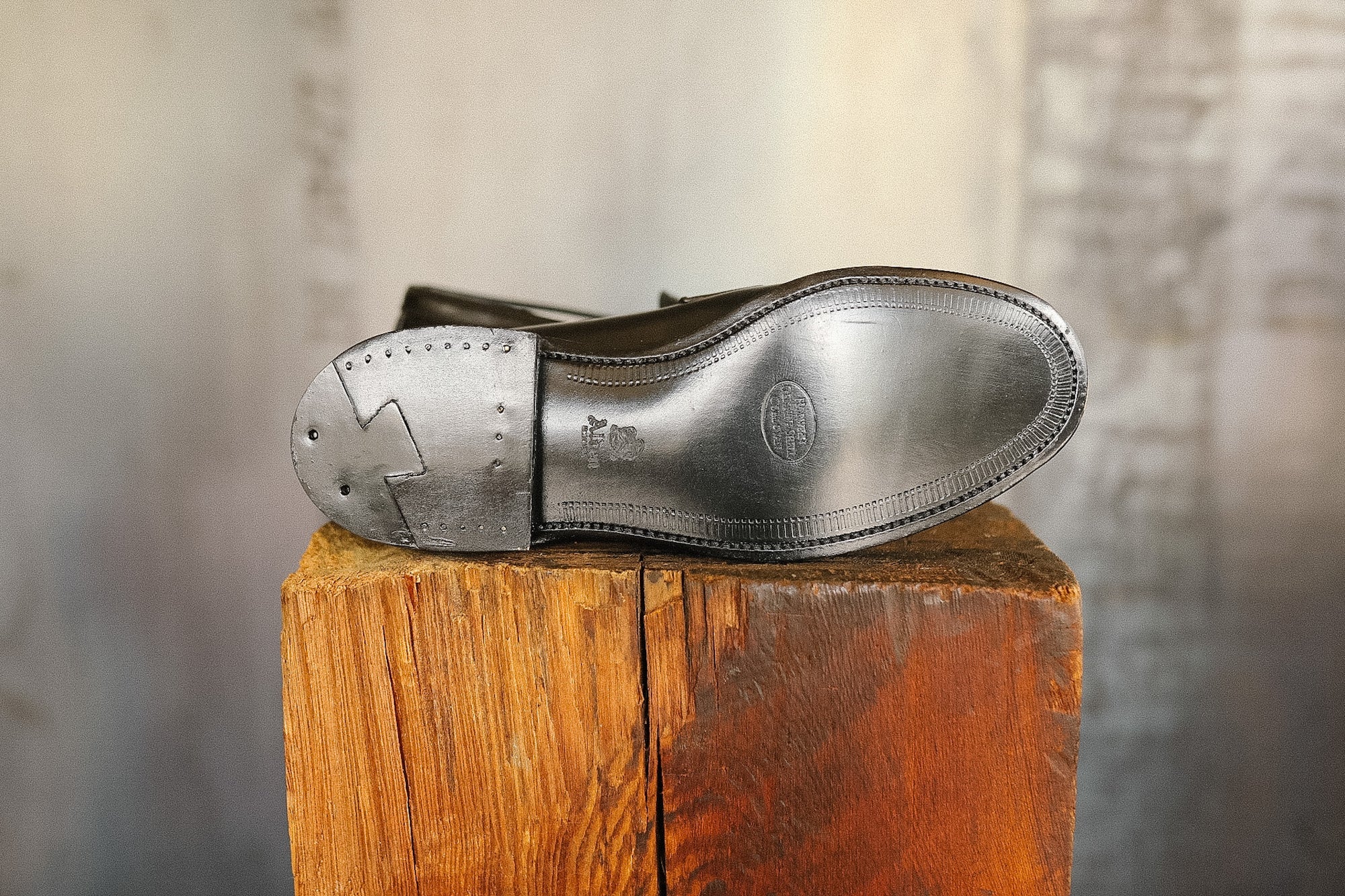 Dark leather shoe with a visible brand logo on a wooden block against a blurred background