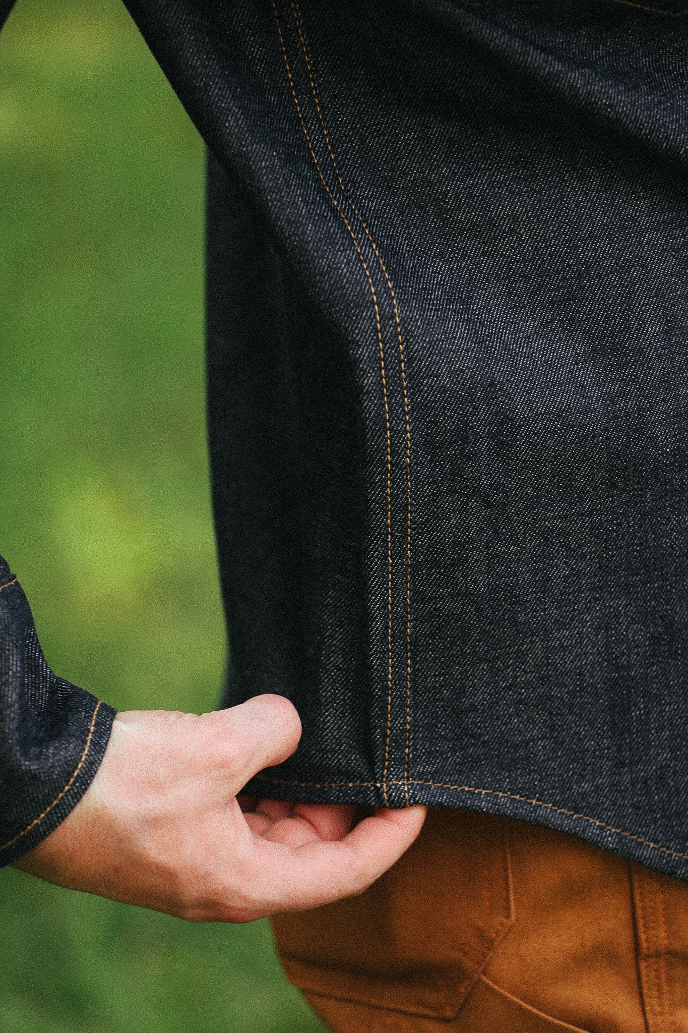 man with denim shirt showing side detail against a green natural background