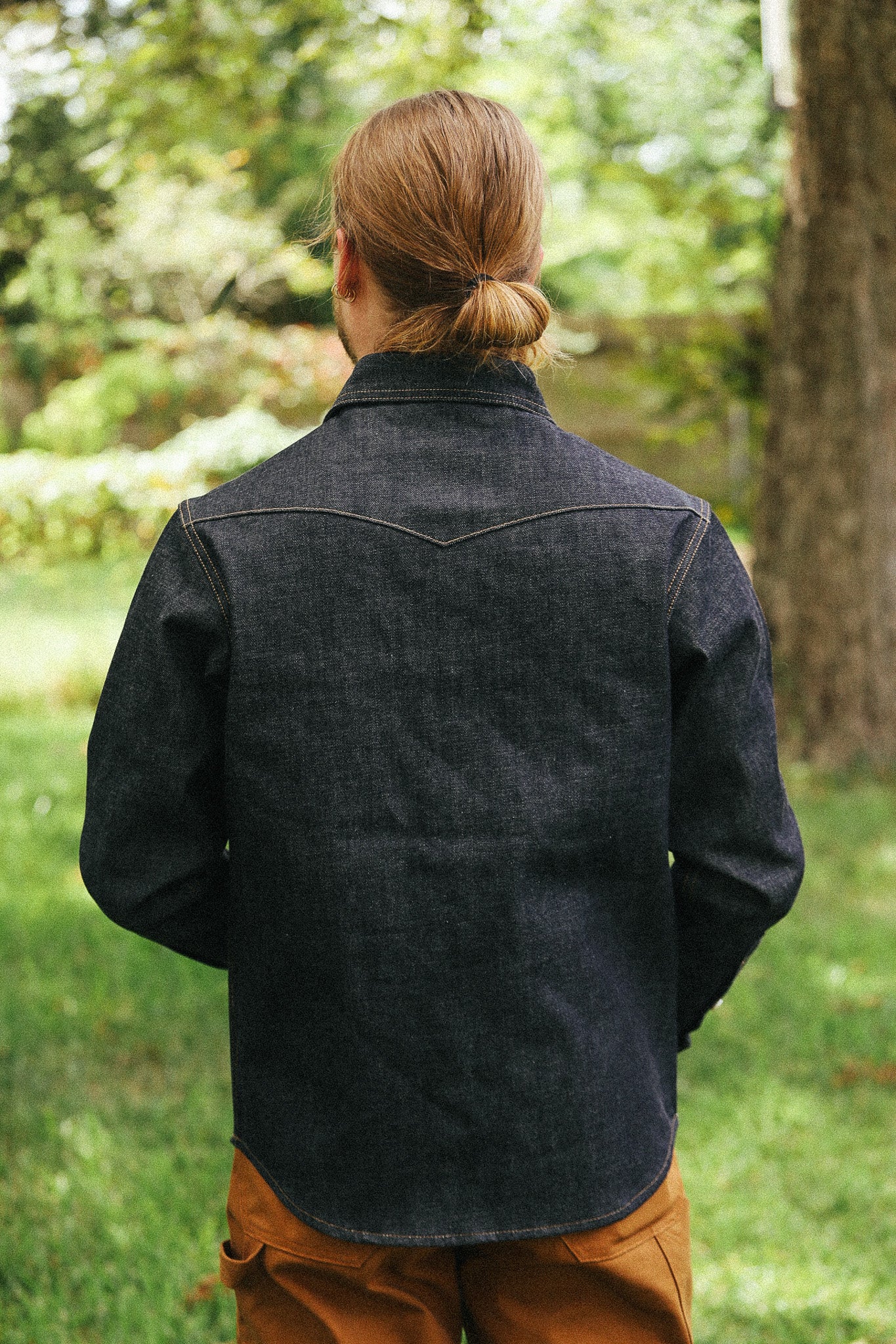 man facing away with denim shirt against a green natural background