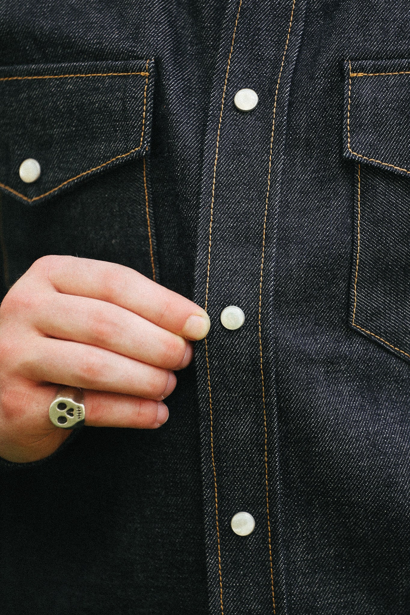man with denim shirt showing snap detail against a green natural background