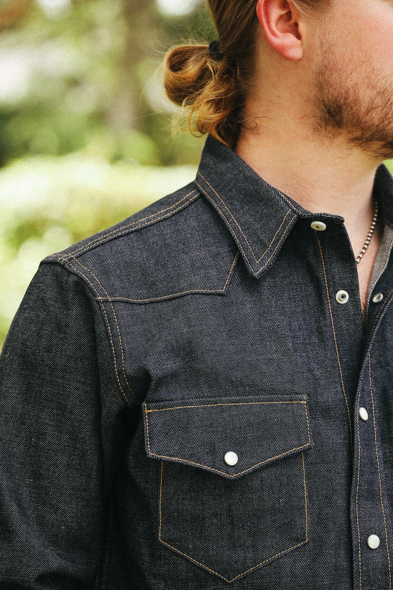 man with denim shirt showing pocket detail against a green natural background