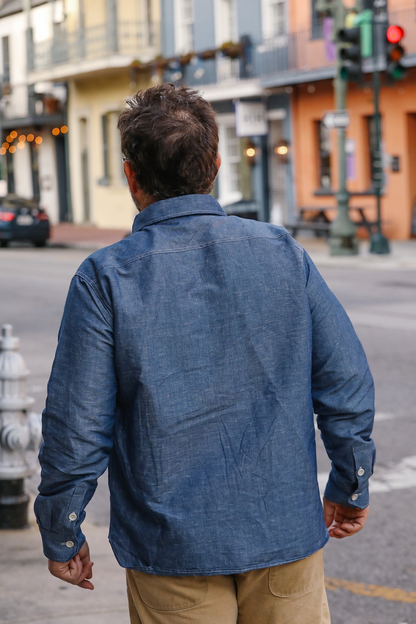 Man wearing a blue denim jacket walking on a city street.