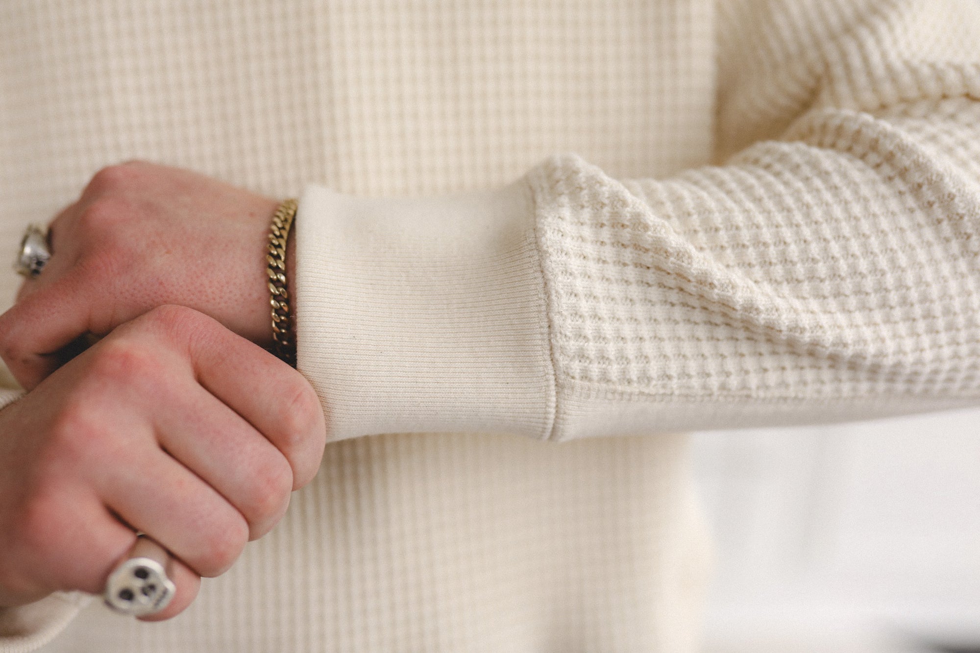 Close-up of a person wearing a textured beige sweater with a focus on the sleeve and hand.