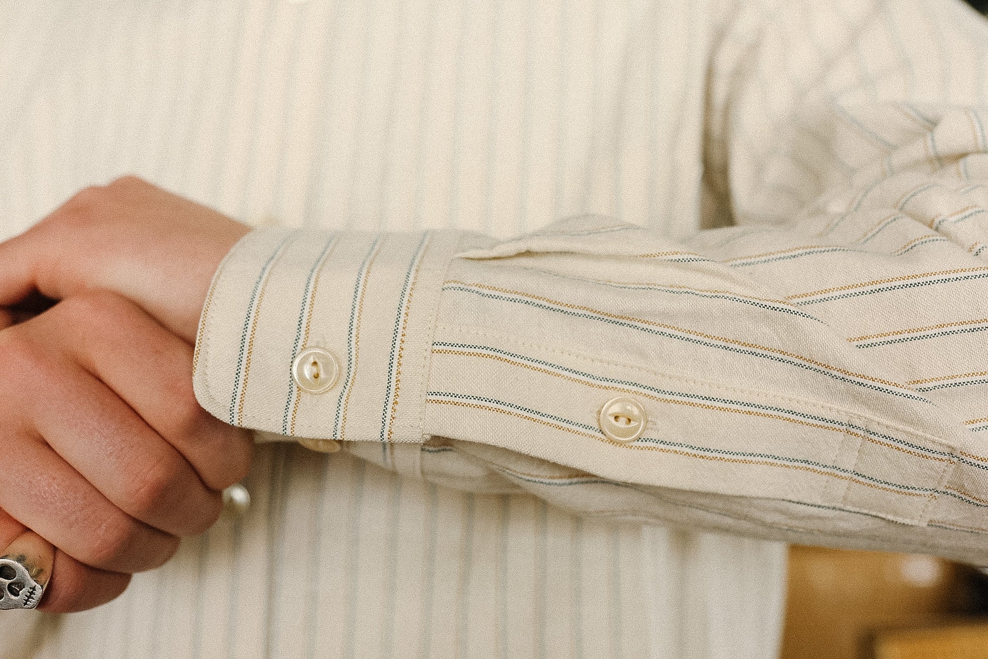 Close-up of a person wearing a beige striped shirt with rolled-up sleeves.