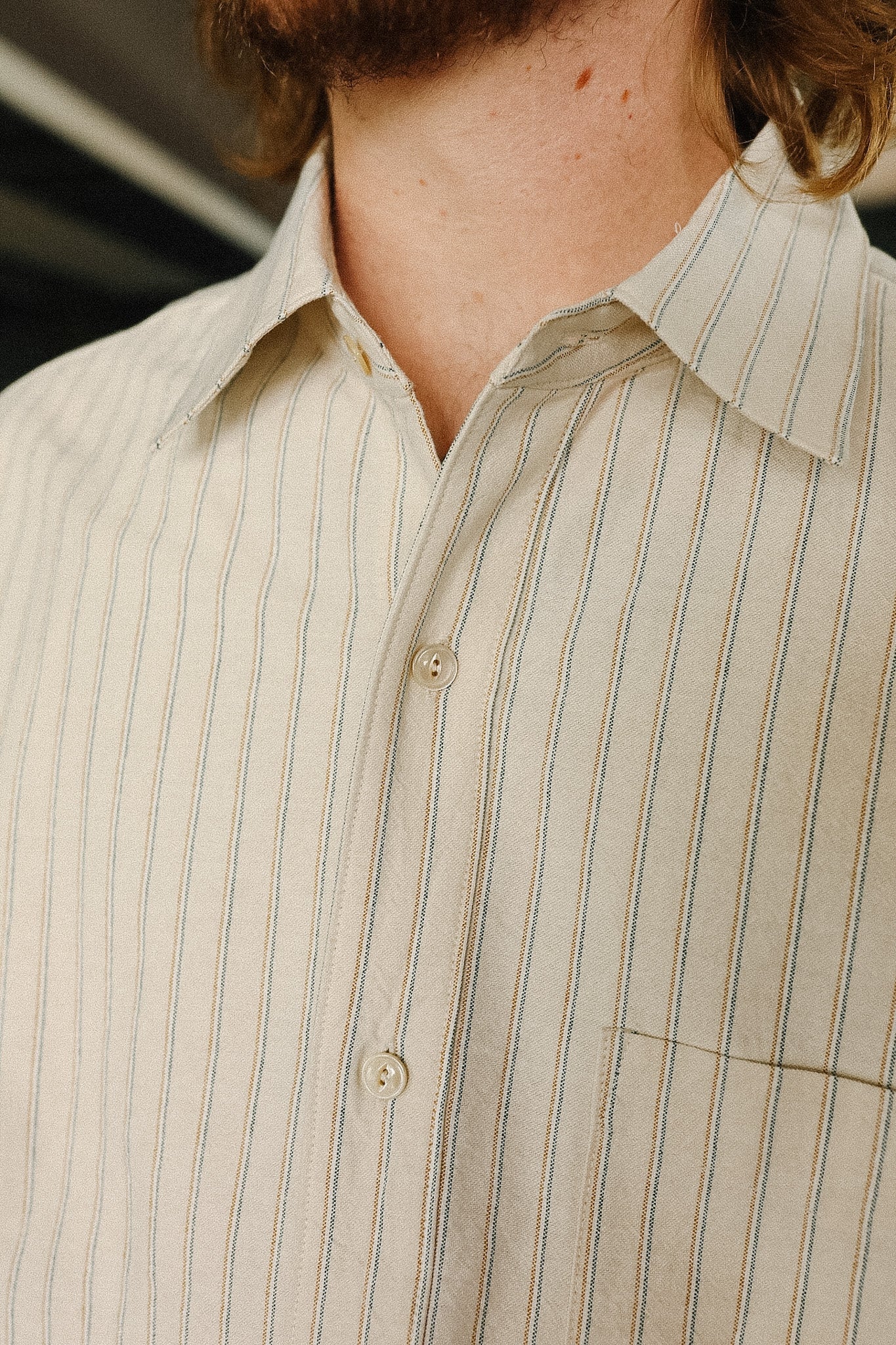 Close-up of a person wearing a beige striped shirt with a blurred background