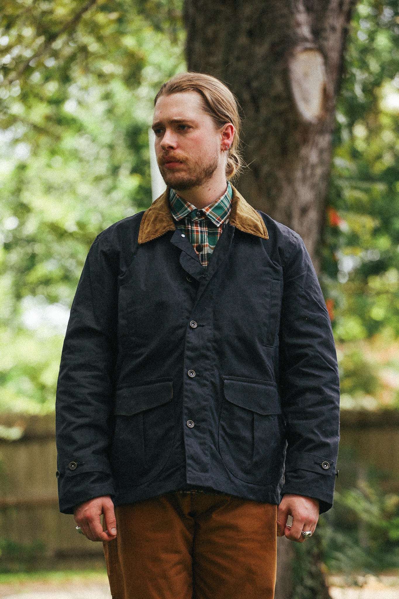 man standing with black jacket and green shirt against a green natural background