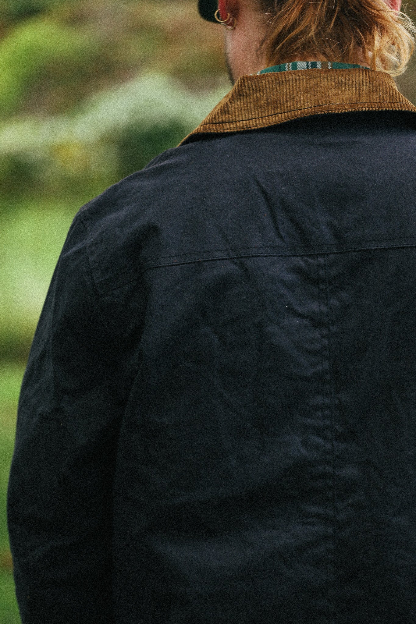 man with black jacket with showing back detail against a green natural background