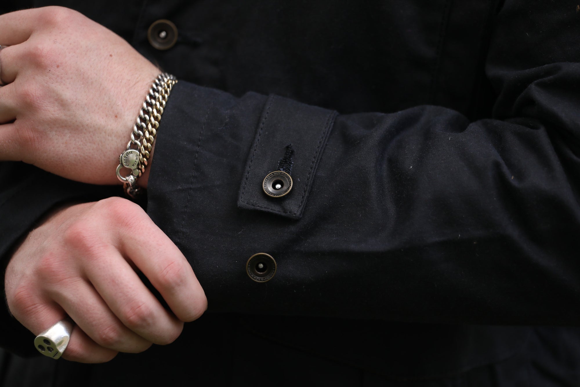 man with black jacket with showing cuff detail against a green natural background