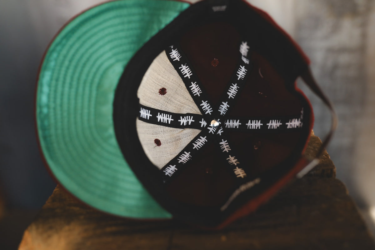Dark maroon baseball cap on a wood block  with interior branding 