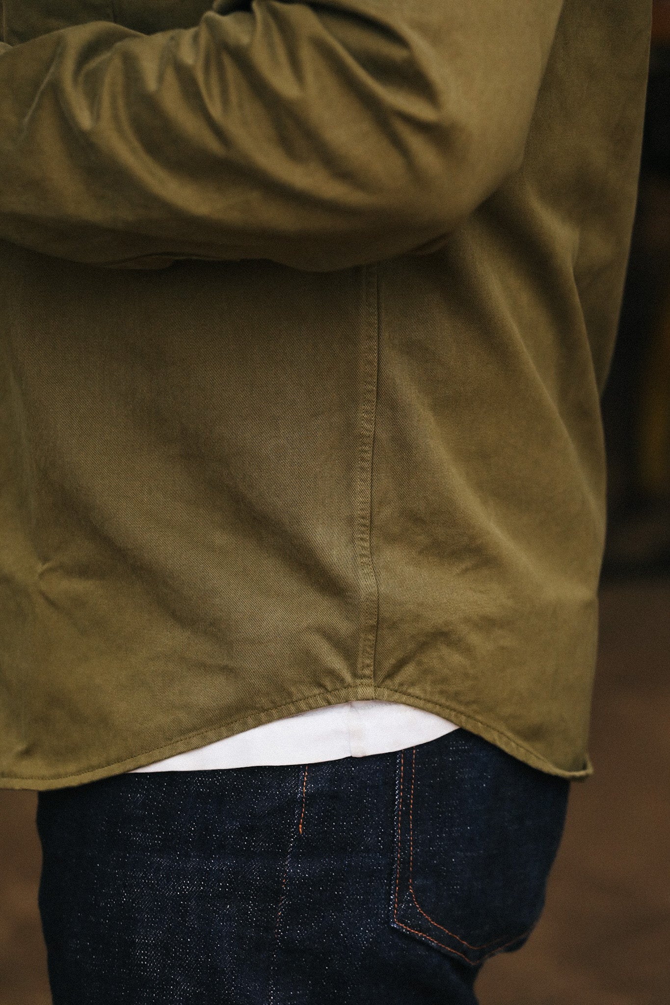 Person wearing a green jacket and dark jeans with a blurred background