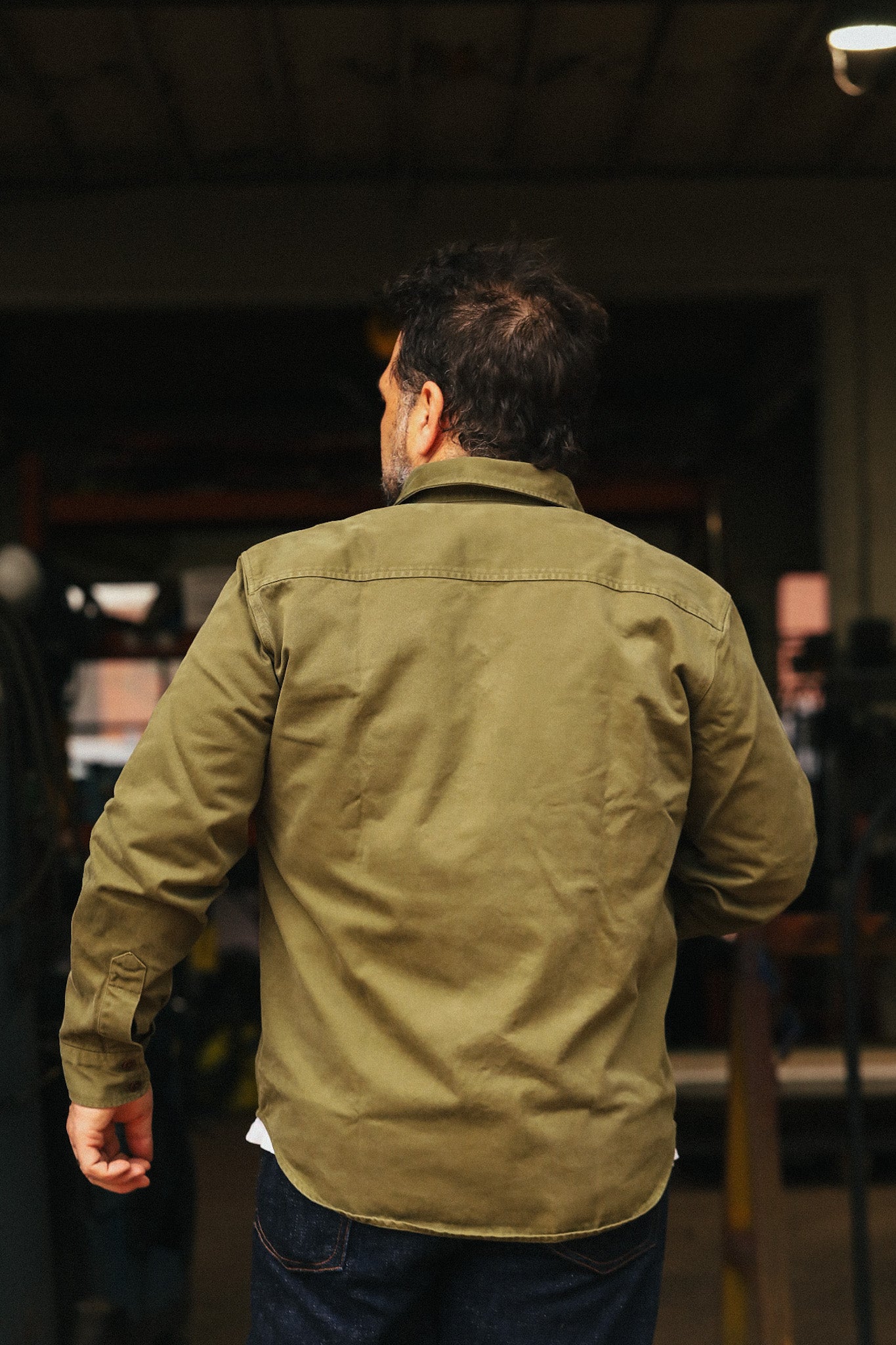 Man wearing a green jacket walking away in an indoor setting