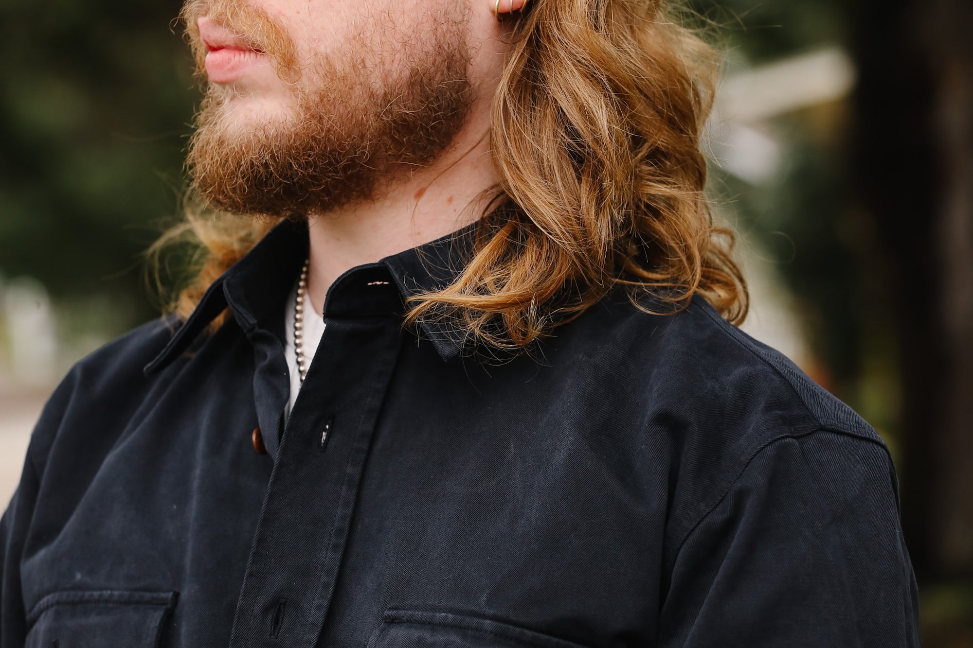 Man with long hair and beard wearing a dark jacket outdoors
