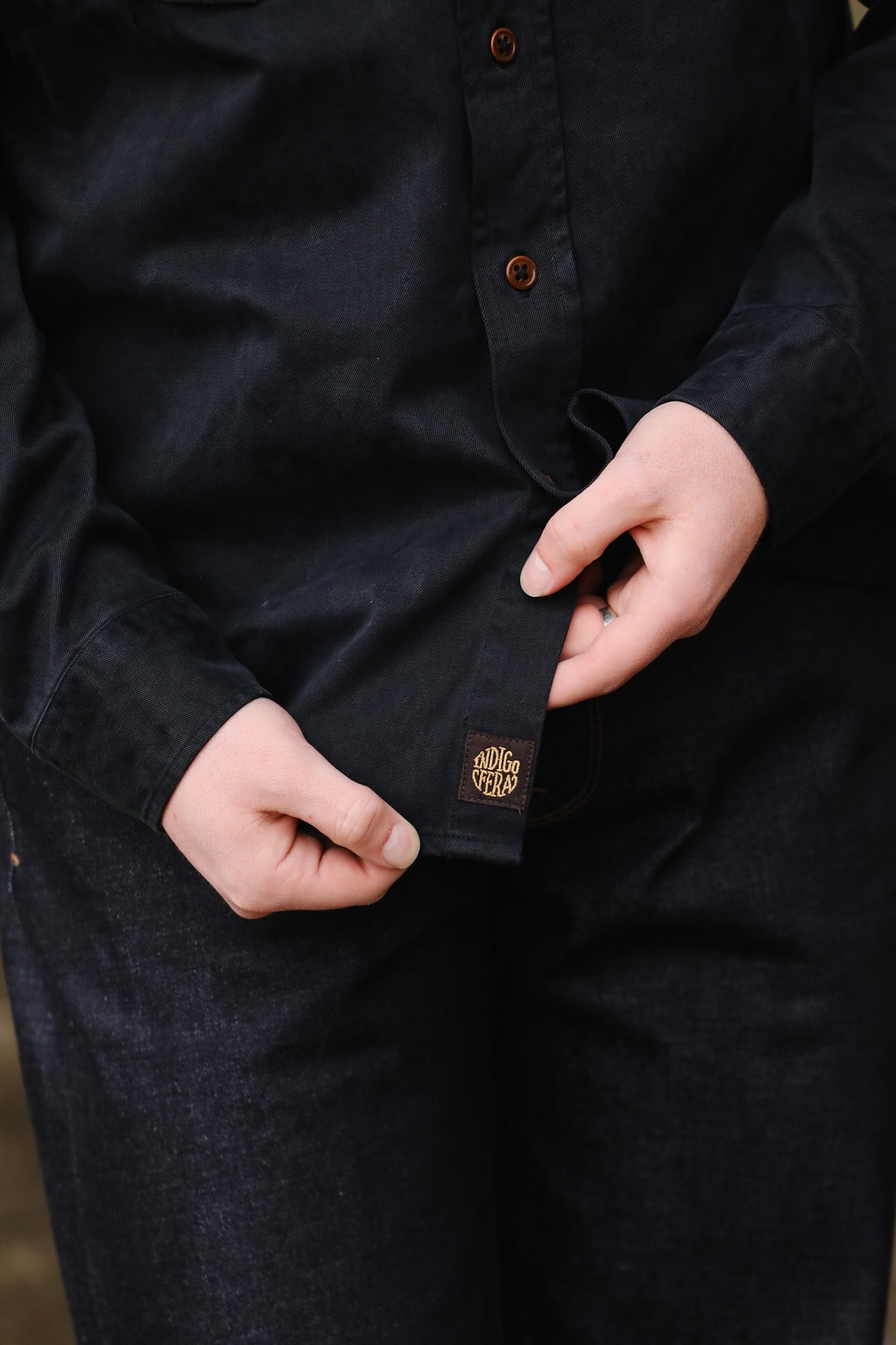 Close-up of a person wearing a black shirt with a brand logo on the chest pocket.