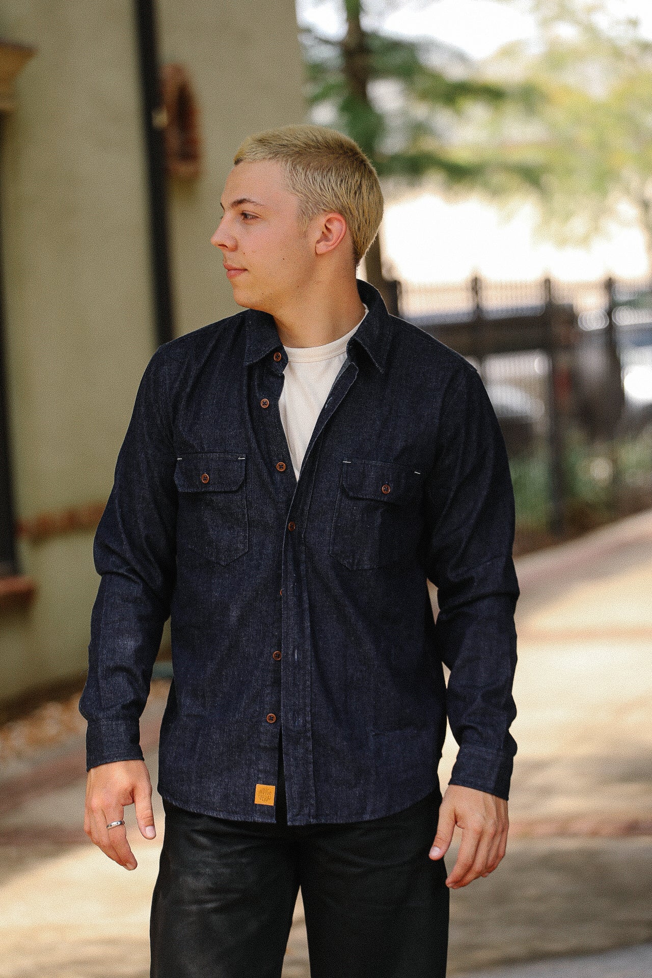 Young man in casual dark denim work shirt and white tee outdoors near building, Iron Shop Provisions style