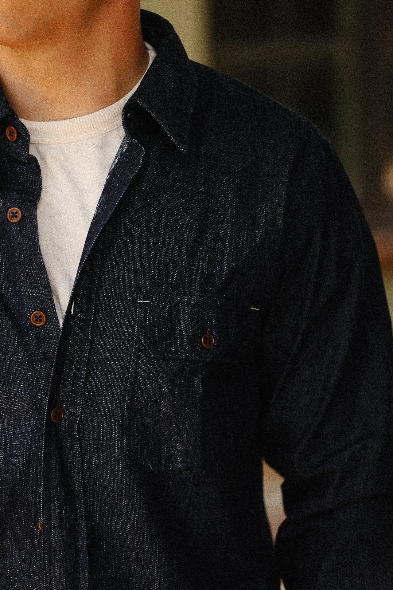 Close-up of a person wearing a dark denim button-up shirt over a white crew neck t-shirt