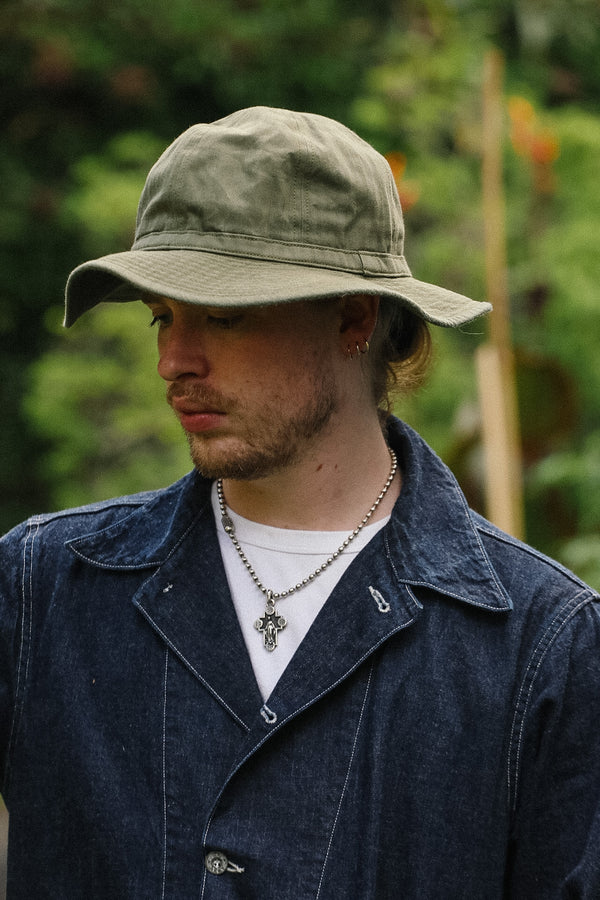Man wearing a beige hat and dark jacket with a blurred natural background