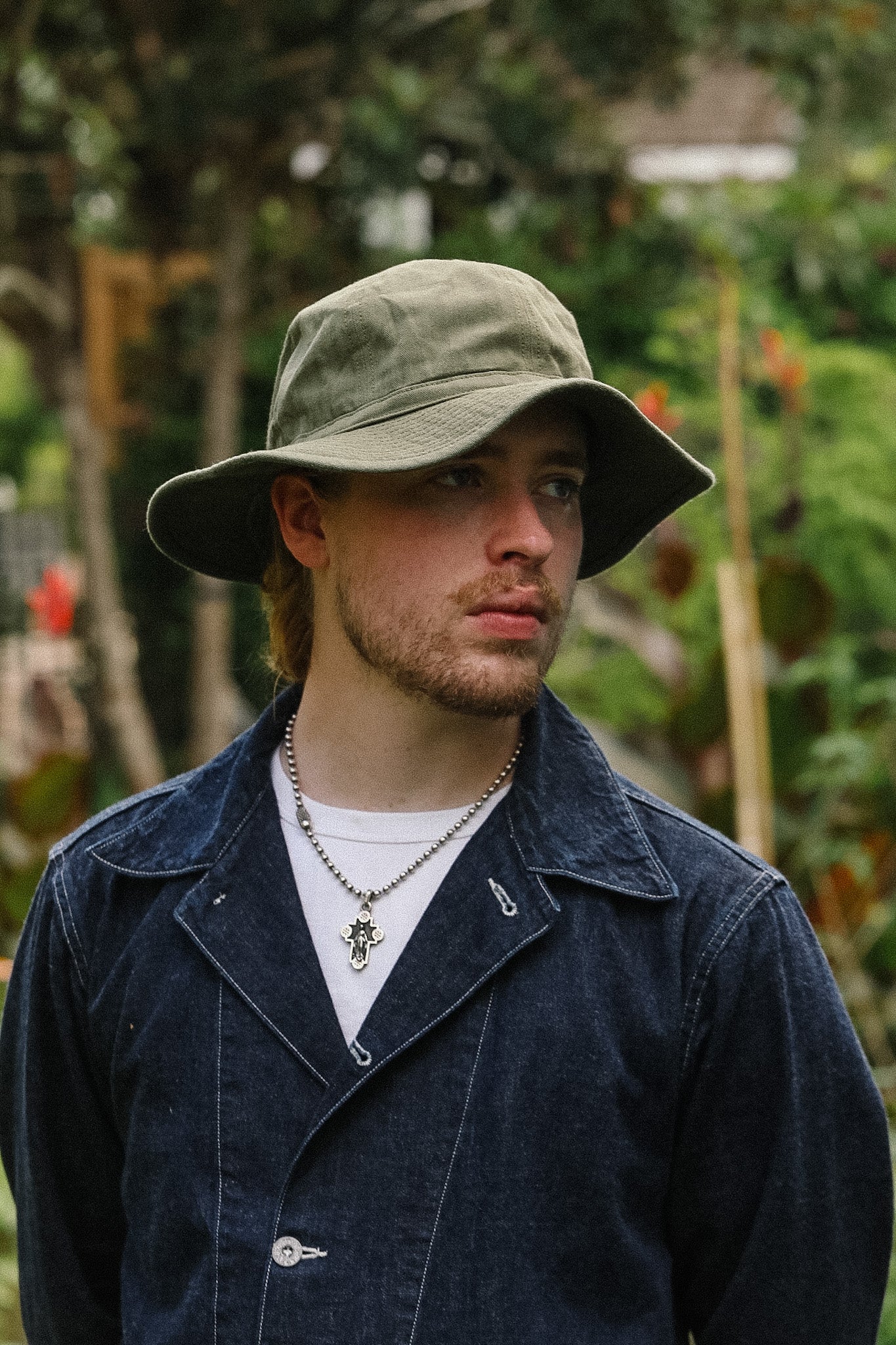 Man wearing a green bucket hat and dark jacket outdoors with blurred background