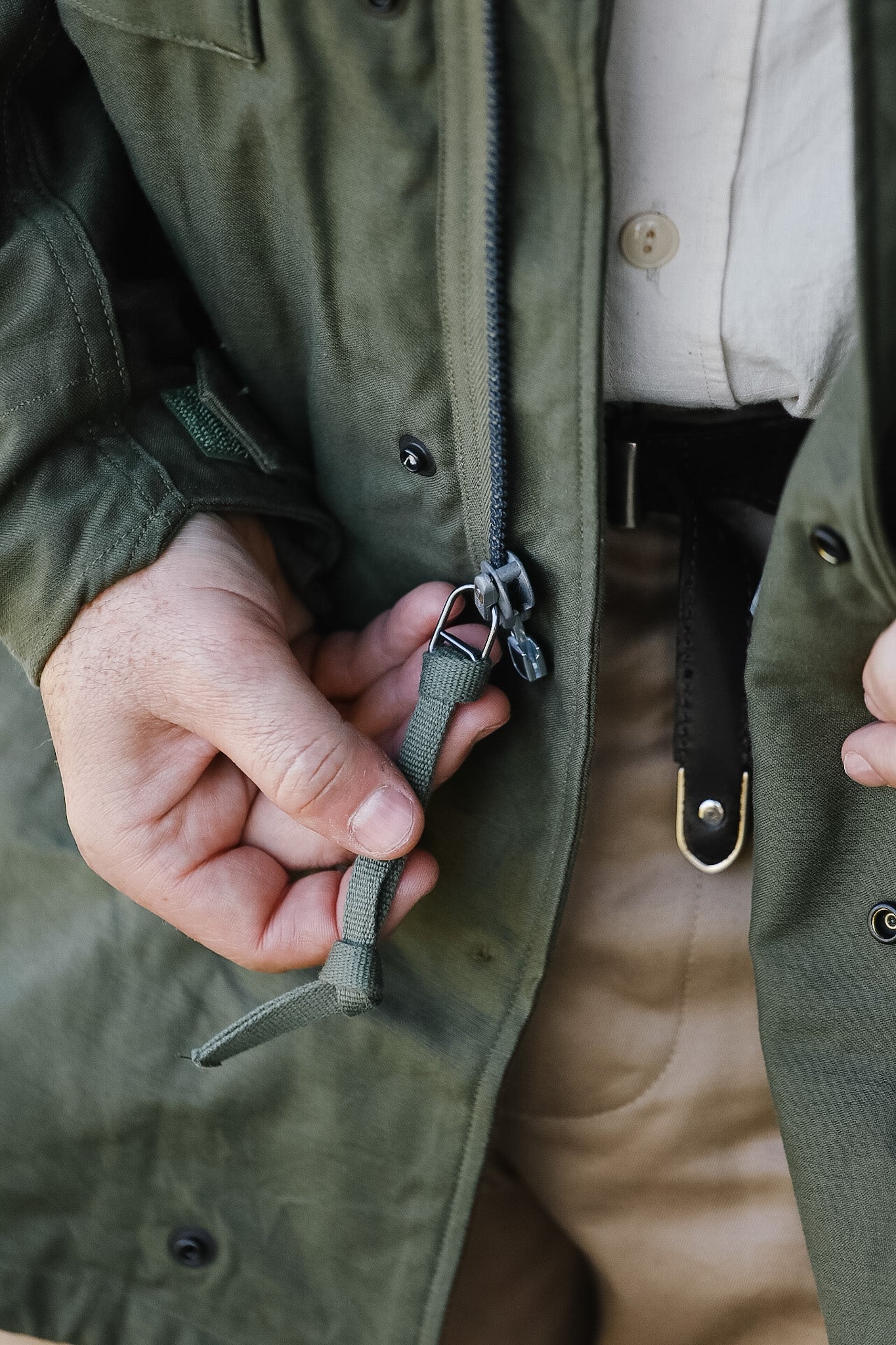 Person adjusting a green jacket zipper with a neutral background