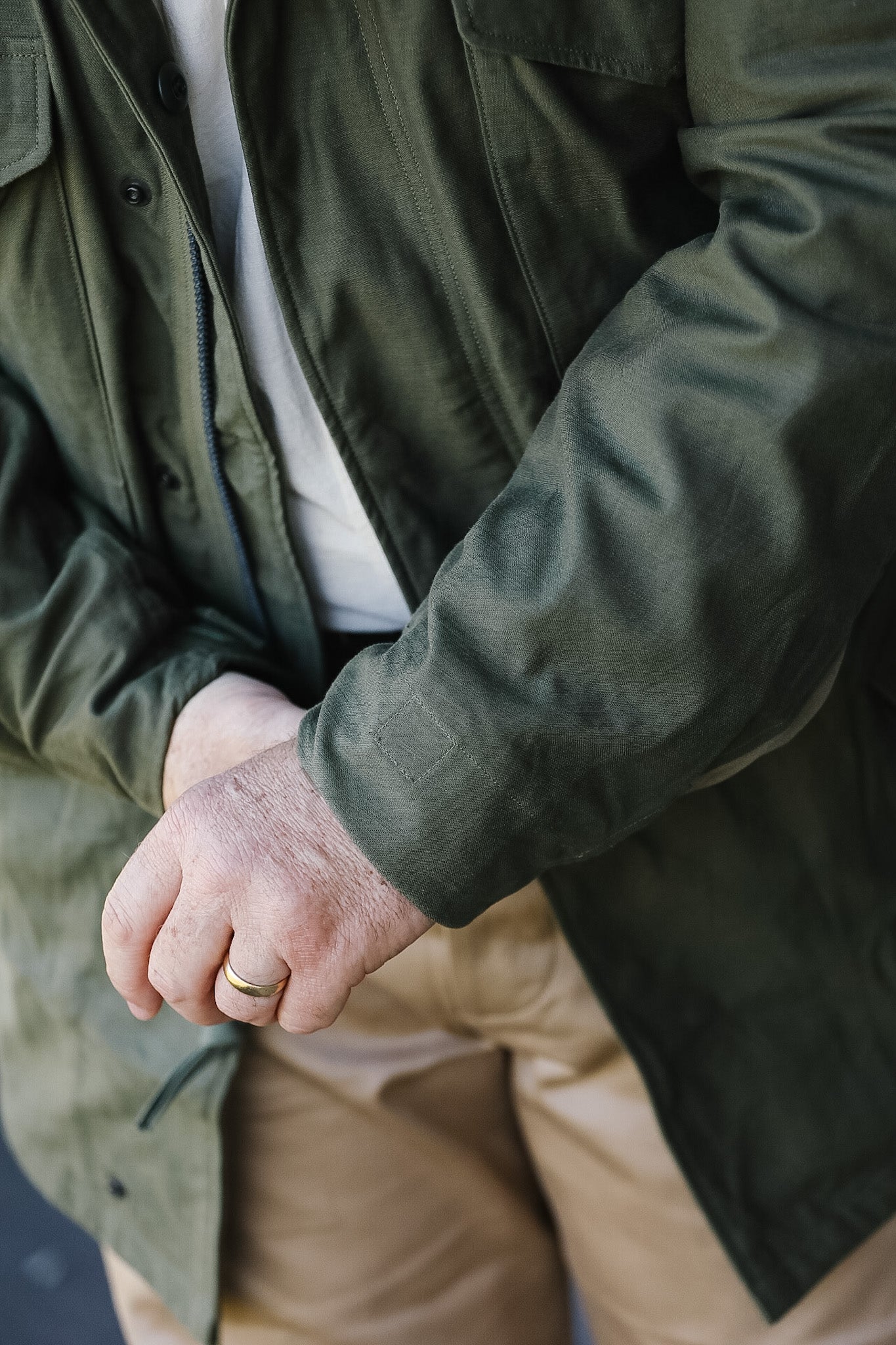 Person wearing a green jacket and beige pants with a close-up of their hand.