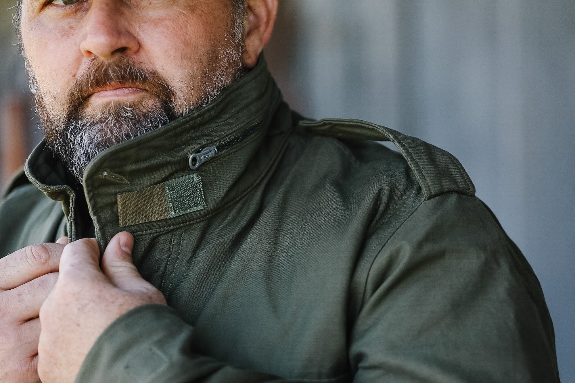 Man wearing a green jacket with a patch, against a blurred background