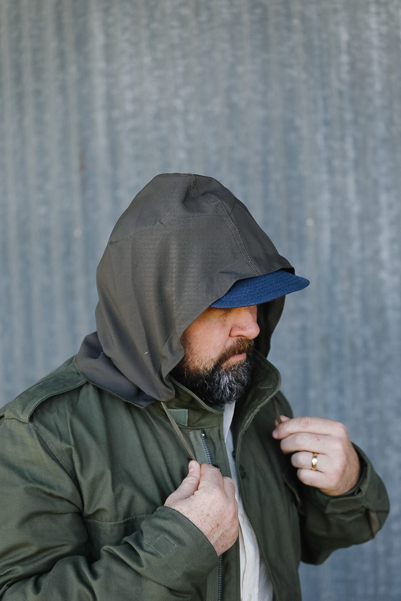 Man wearing a green jacket with a hood against a gray corrugated metal background
