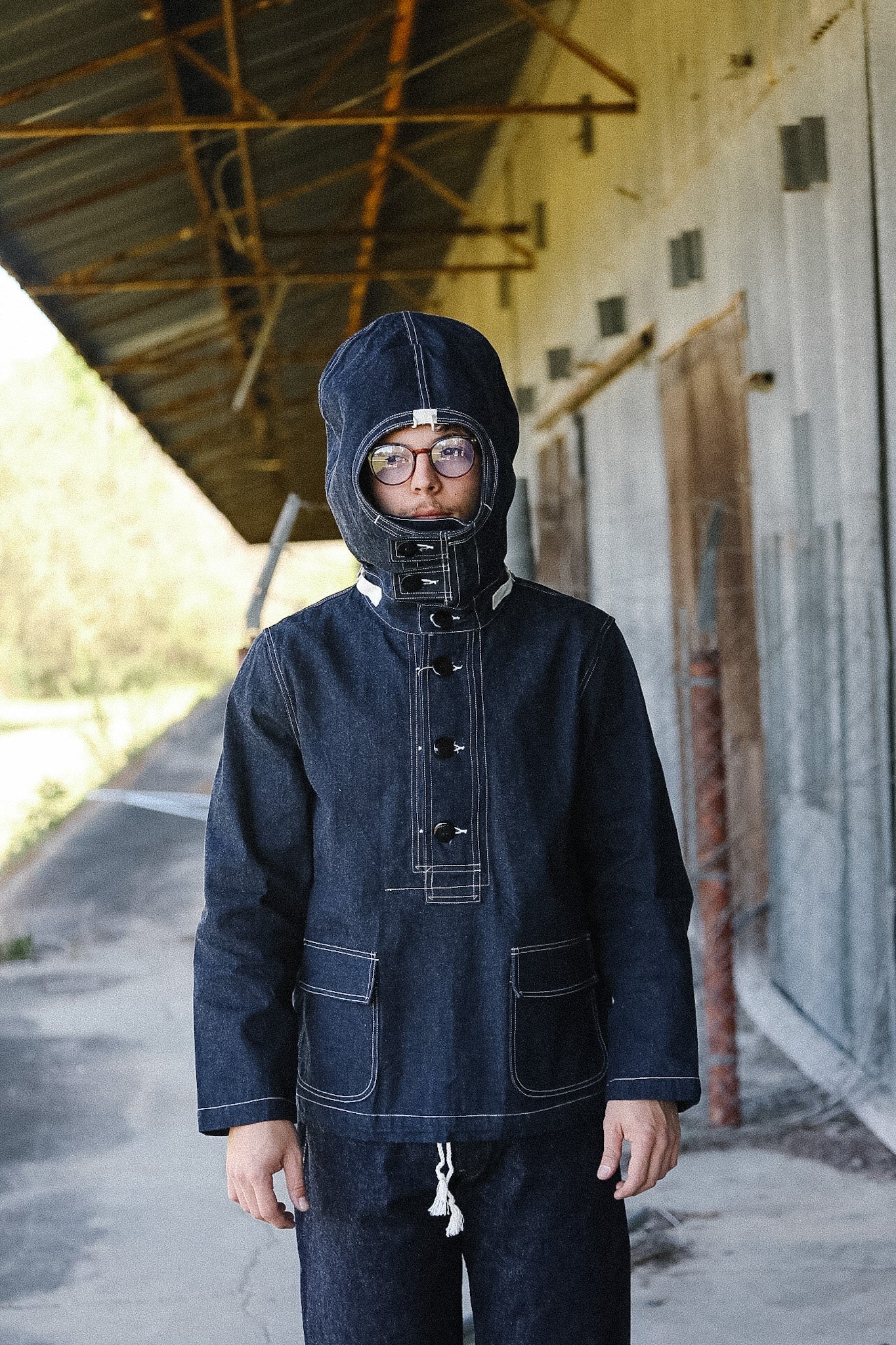 Person wearing a dark blue hooded coat in an industrial setting