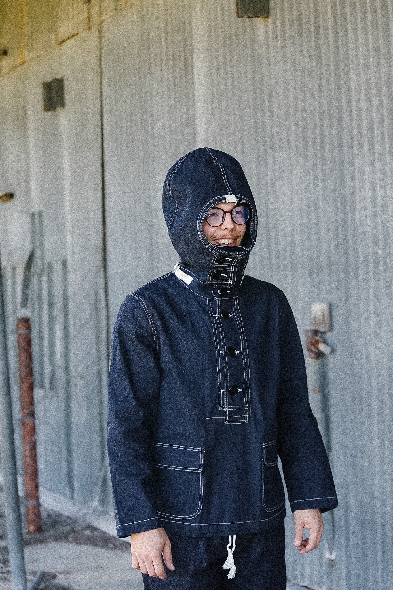 Person wearing a dark blue hooded jacket in front of a textured wall.