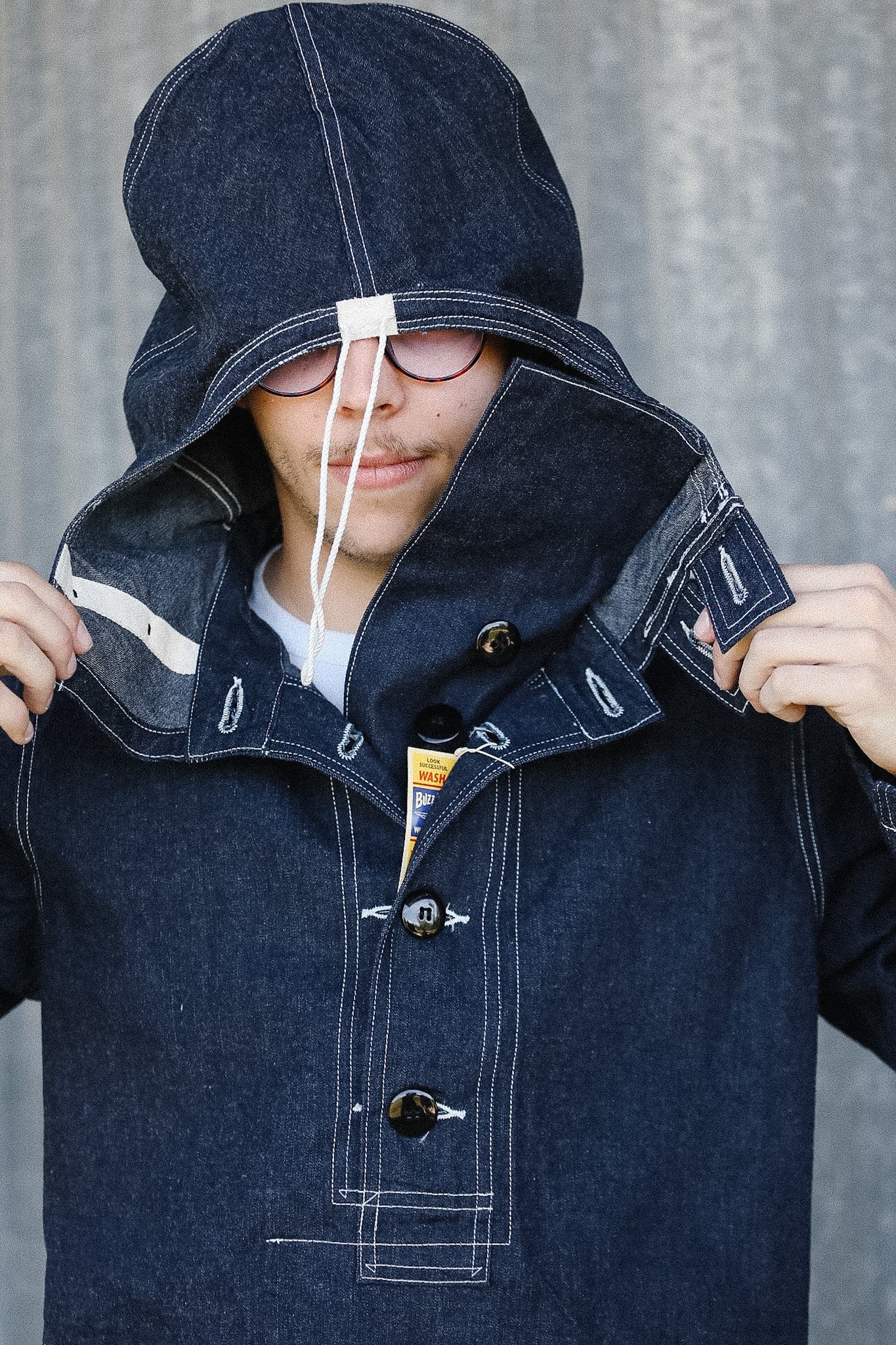 Person wearing a dark blue hooded coat against a gray background