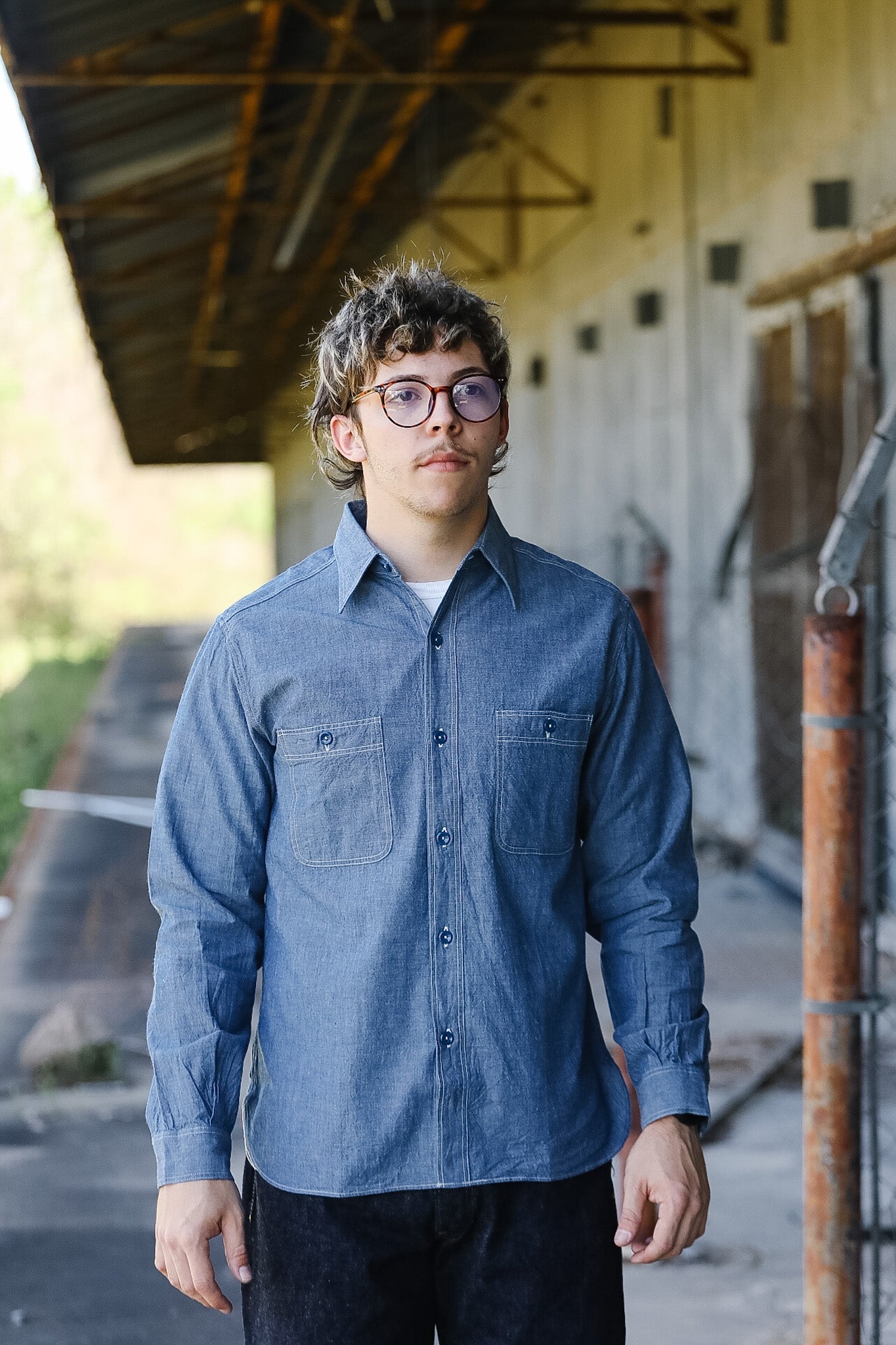 Man wearing a blue shirt standing in an outdoor setting with a building in the background