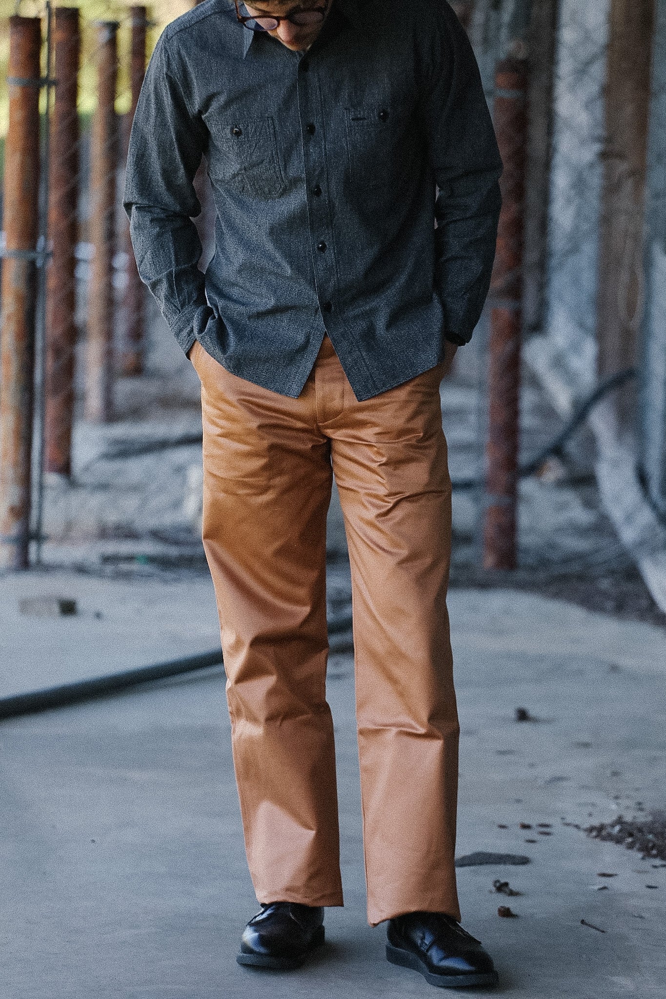 Person wearing a dark shirt and brown pants standing in an industrial setting.