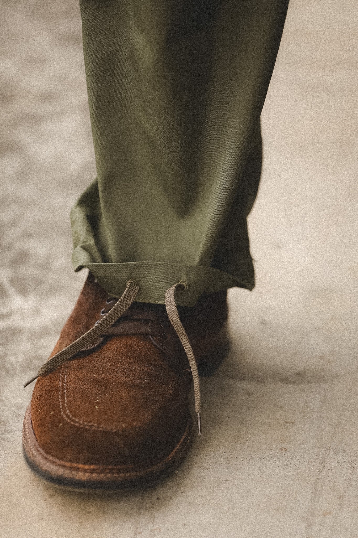 Brown suede shoes with green pants on a concrete floor
