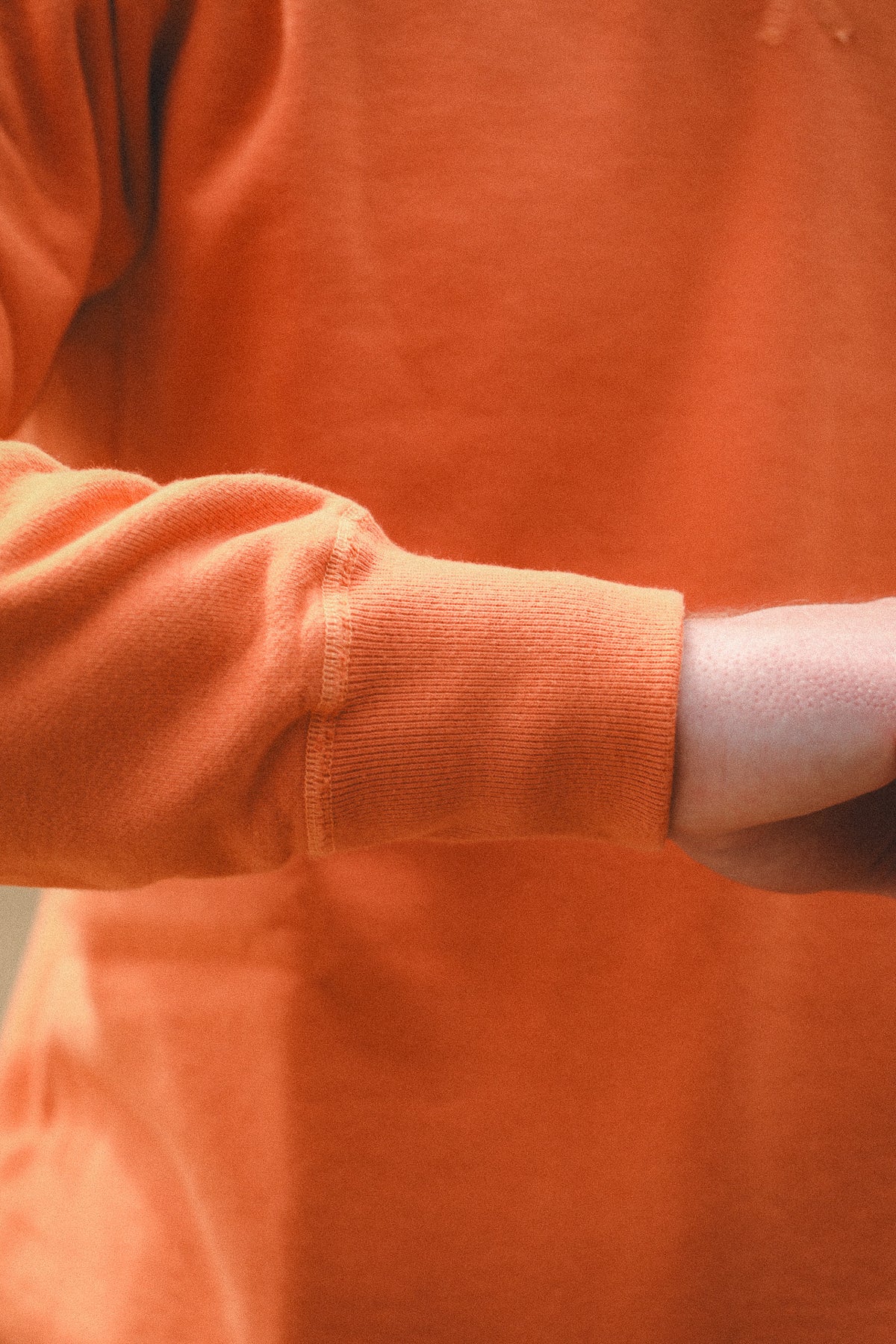 Close-up of a person wearing a bright orange long-sleeve top, showing the ribbed cuff and part of the arm.