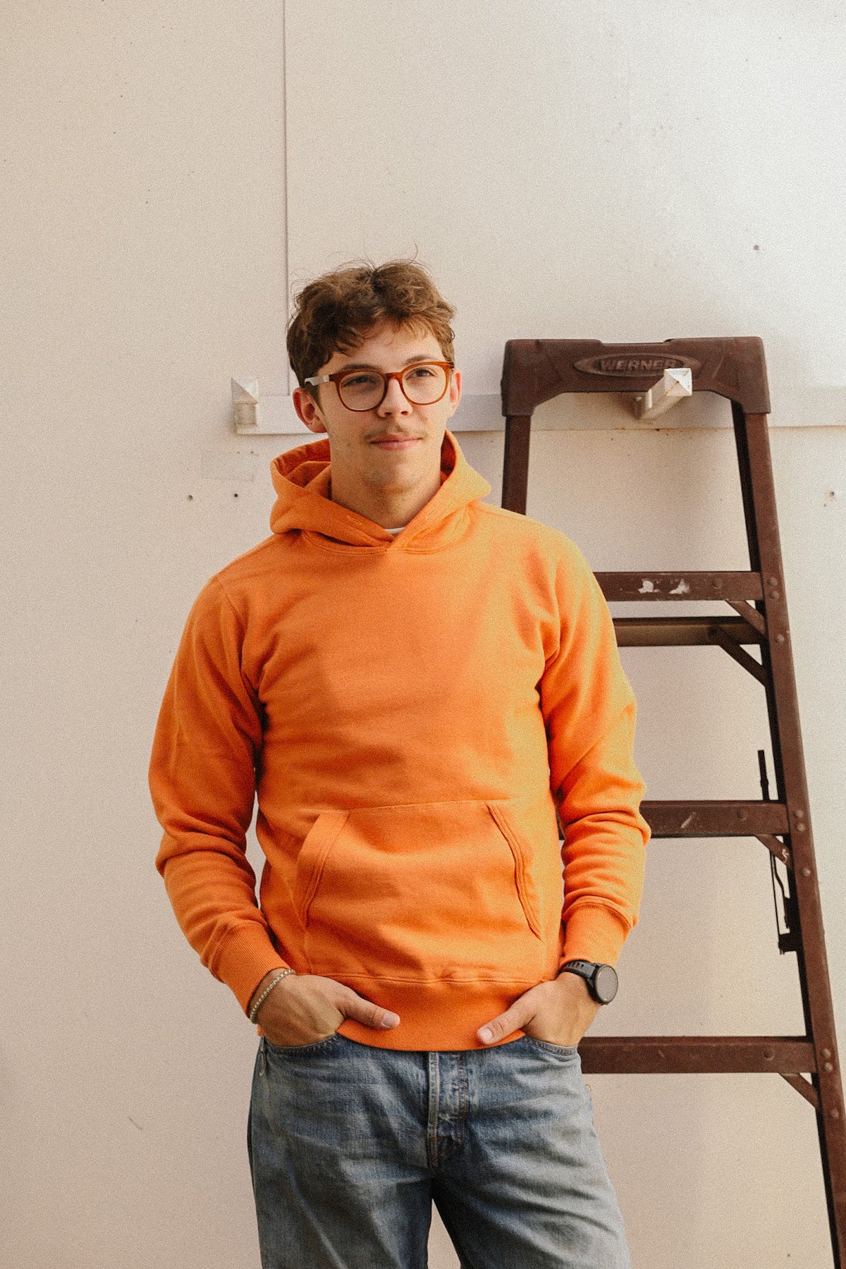 man wearing an orange sweater and jeans on a white backdrop