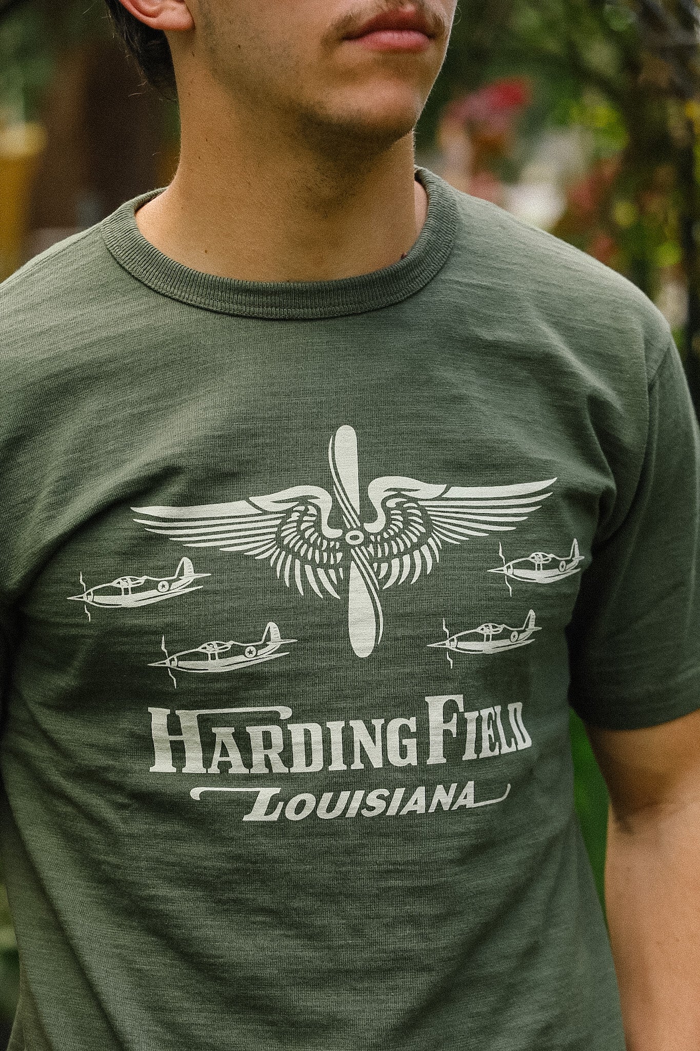 Person wearing a green t-shirt with airplane graphic and text